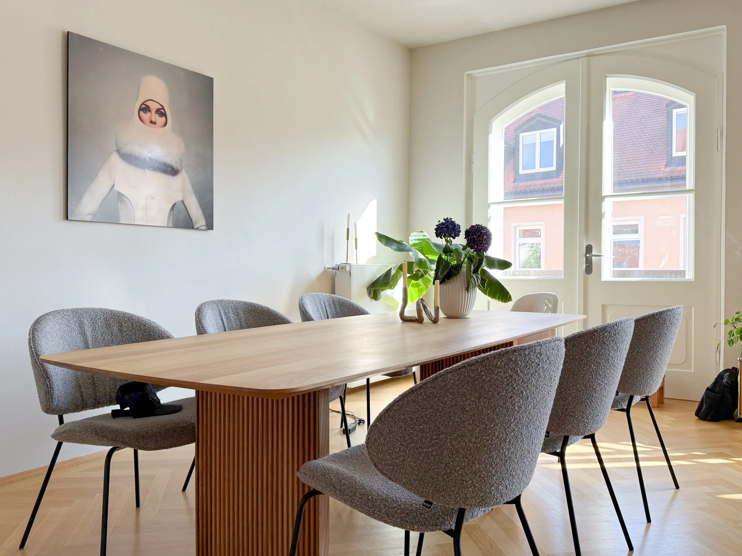 Essbereich mit Holztisch, freifrau Stühlen und Kunst – ruhige, moderne Einrichtung vor klassischer Altbaukulisse in München.