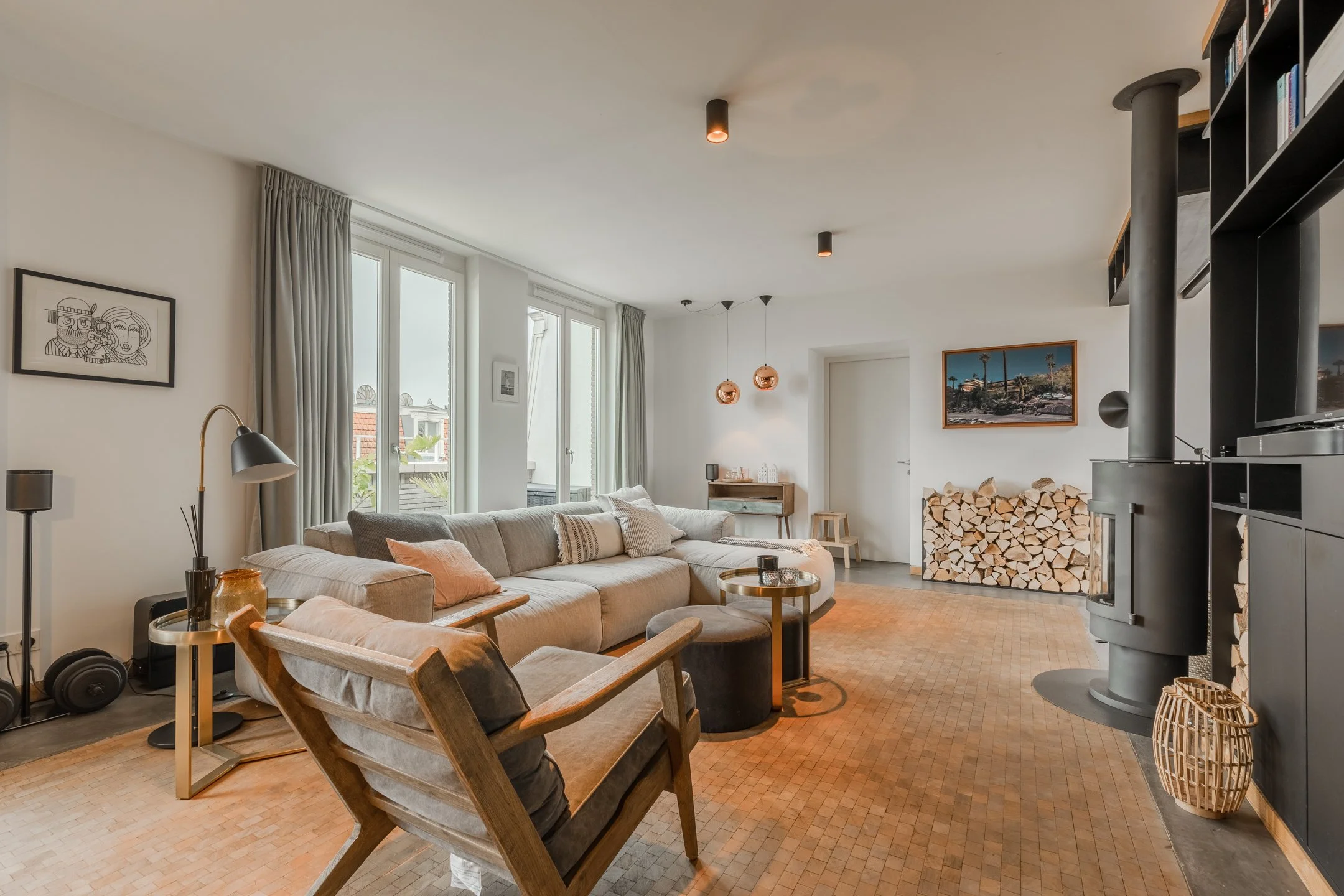 Großzügiges Wohnzimmer mit Kaminofen, Holzfußboden und maßgefertigten dunklen Einbauten – warmes, urbanes Interior Design.