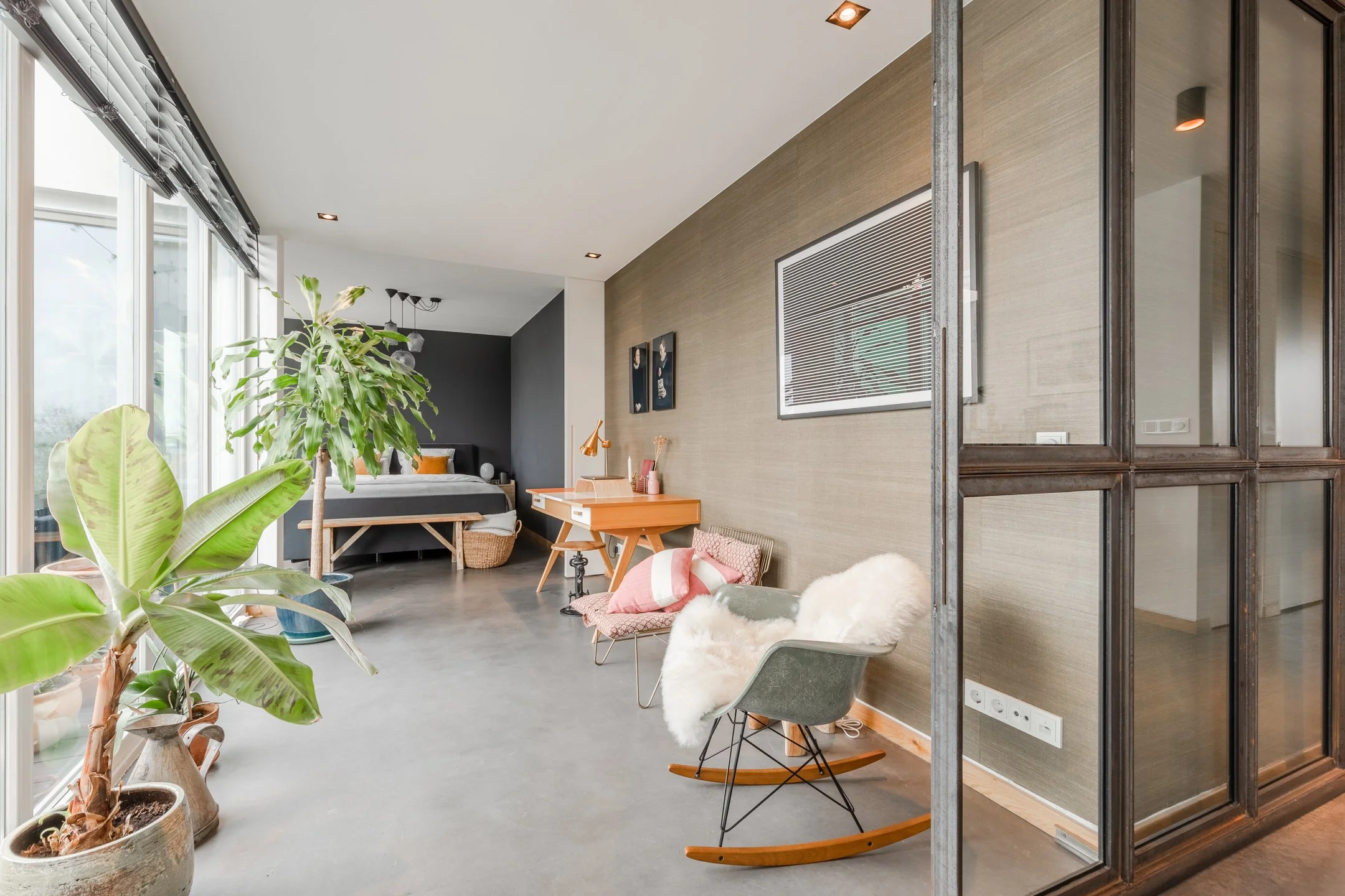 Arbeitsbereich mit Betonboden, strukturierter Wandgestaltung, Vintage-Schreibtisch und vielen Pflanzen im Penthouse in Amsterdam.