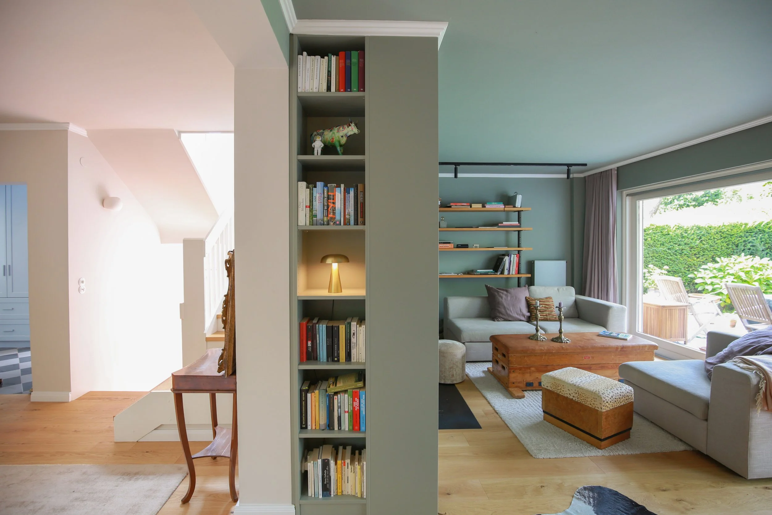 Interior Design eines Wohnbereichs in Hamburg mit maßgefertigtem Einbau, integriertem Bücherregal und Farbkonzept in gedeckten Grün- und Rosétönen.
