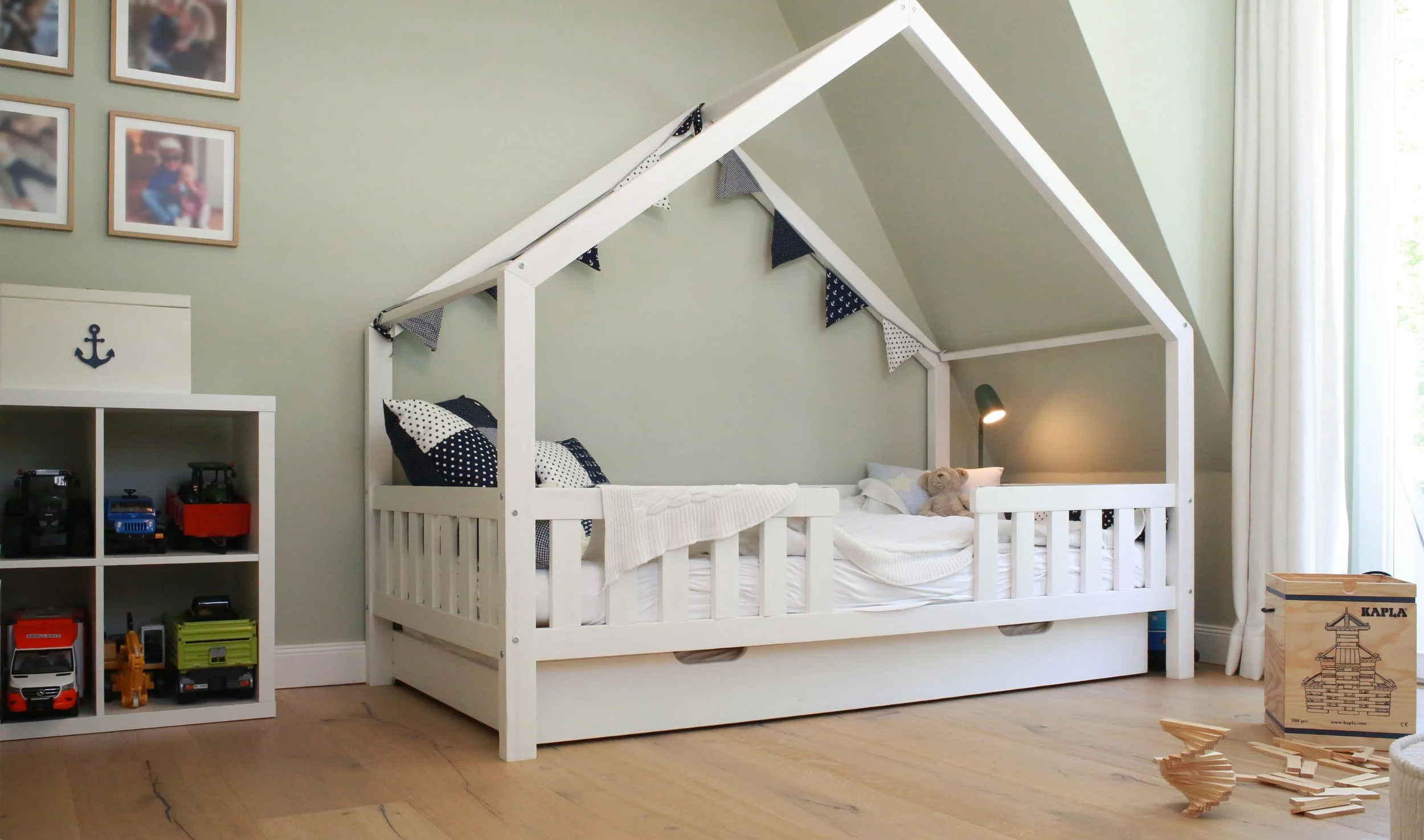 Kinderzimmer mit Hausbett, gedecktem Grün-Grau und natürlichen Holztönen – ruhige, kindgerechte Raumgestaltung mit Charakter.