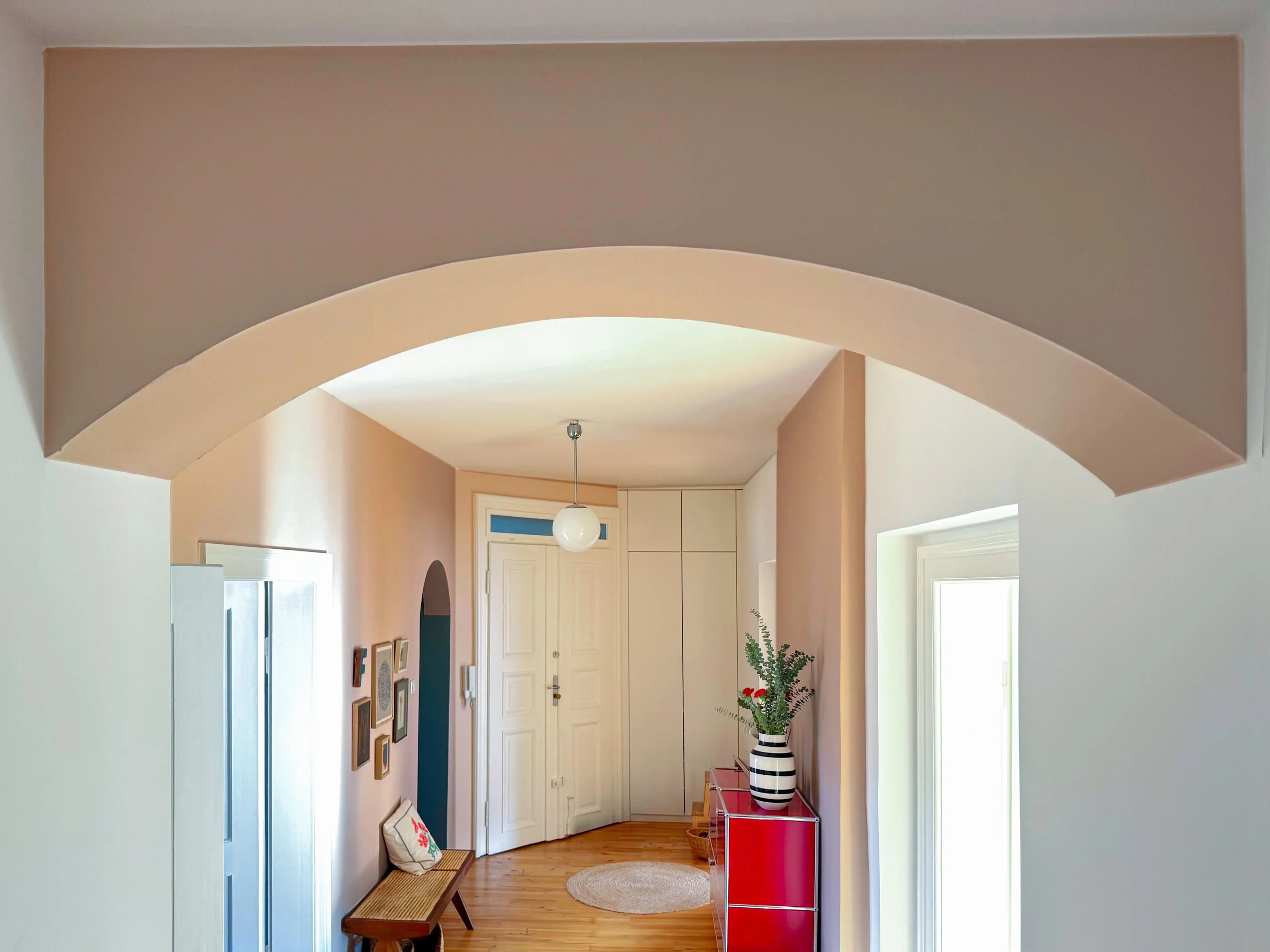 Altbauflur mit Rundbogen, Rosé-Tönen und farbig akzentuiertem Durchgang – individuelles Farbkonzept für eine Wohnung im Münchner Glockenbachviertel.