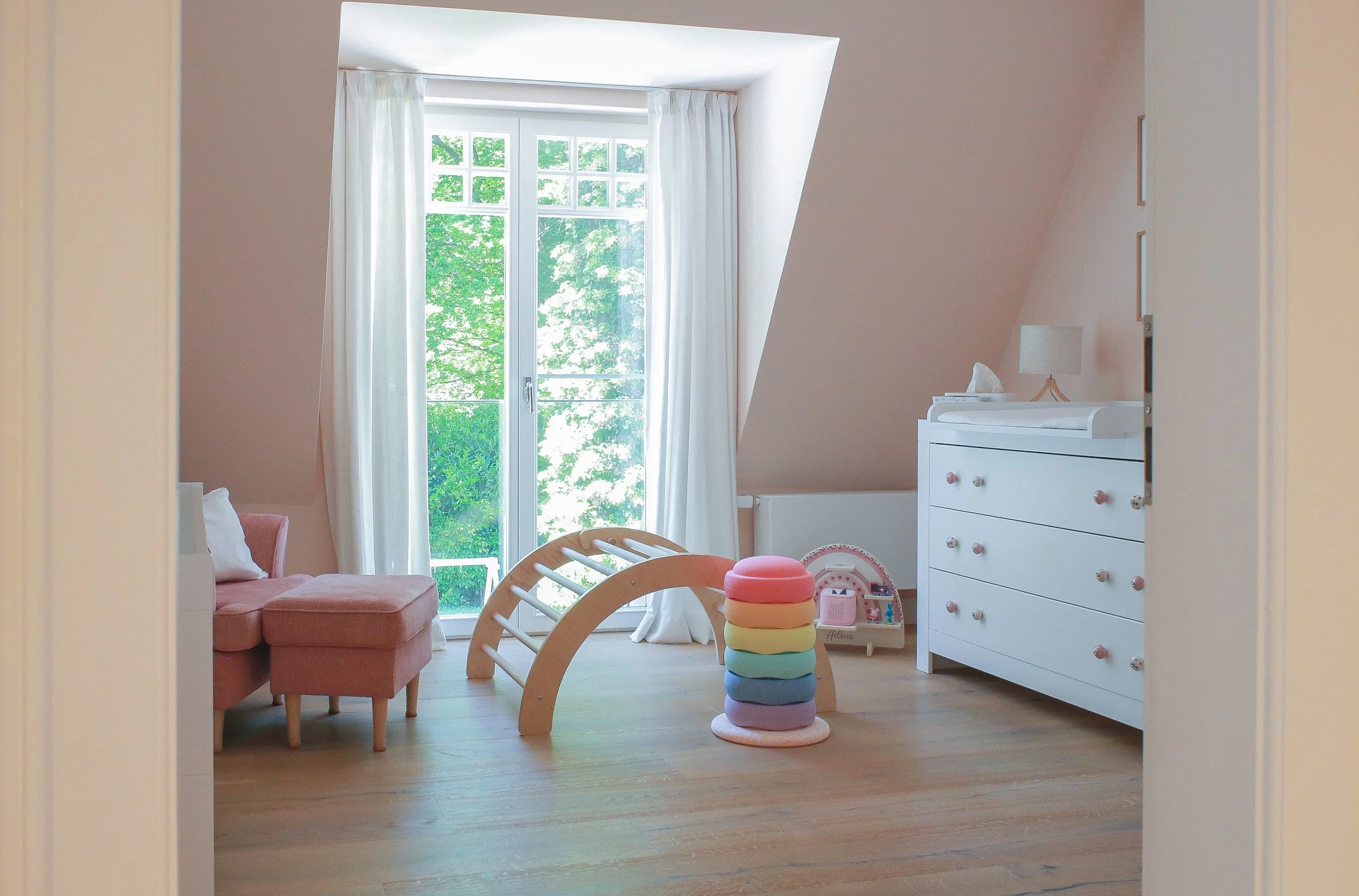 Kinderzimmer mit sanften Rosé-Tönen an Wänden und Dachschrägen, natürlichen Materialien und verspielten Farbakzenten.