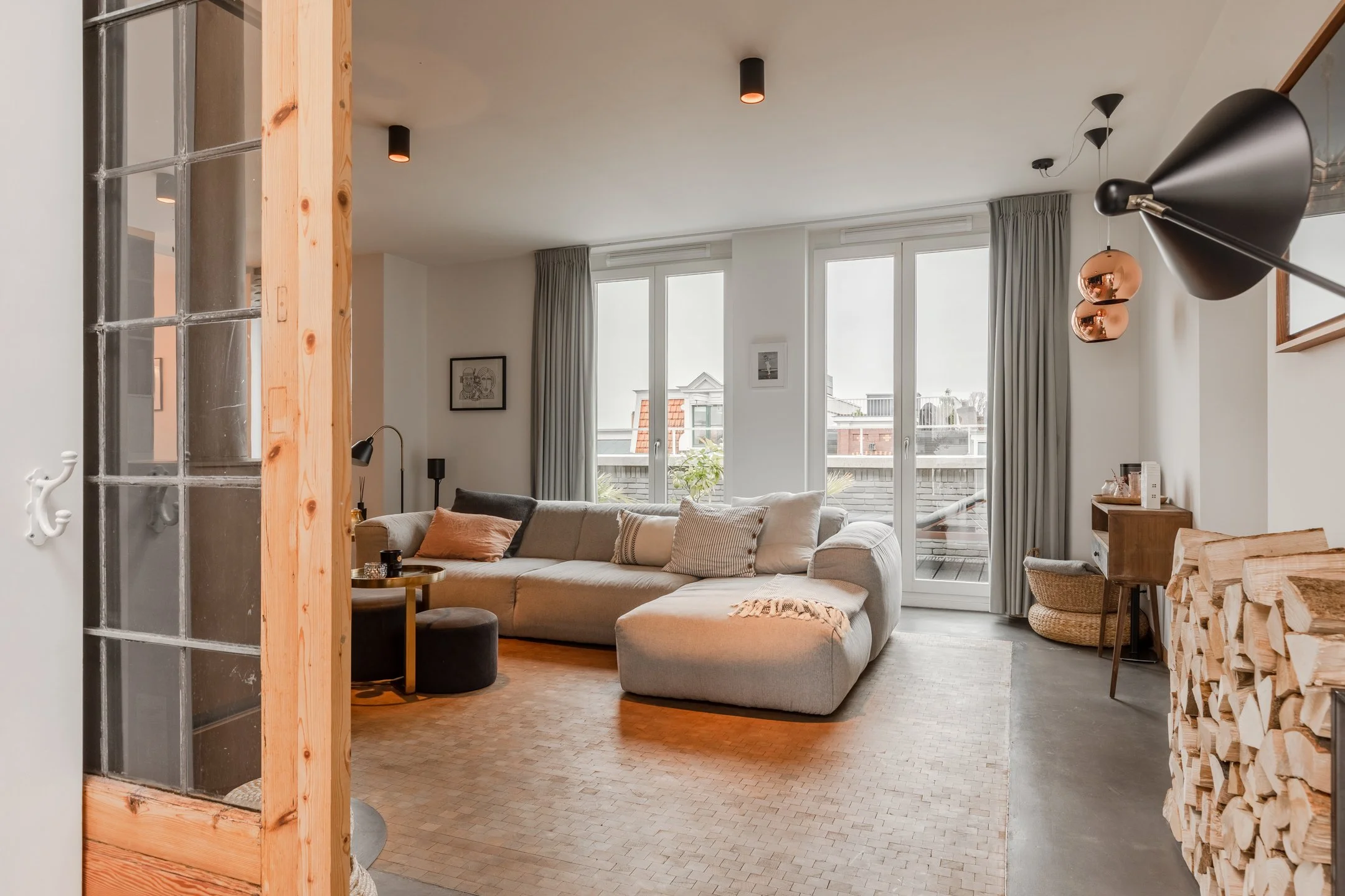 Wohnbereich eines Penthouses in Amsterdam mit Betonboden, Holzparkett, großen Fensterflächen und warmen Interior-Details.