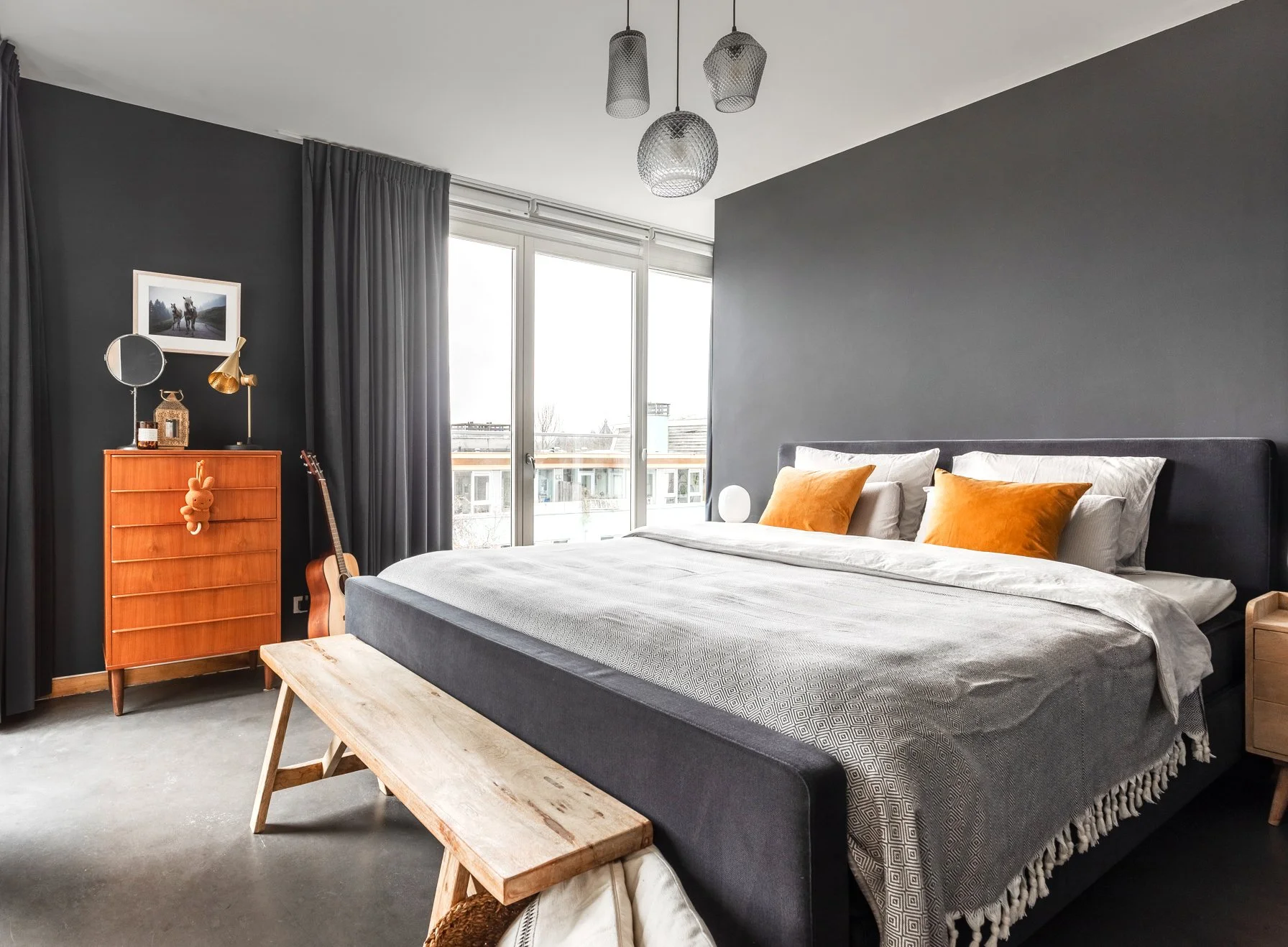 Schlafzimmer mit dunklem Farbkonzept, Vintage-Kommode, warmen Holzakzenten und zurückhaltender Einrichtung.