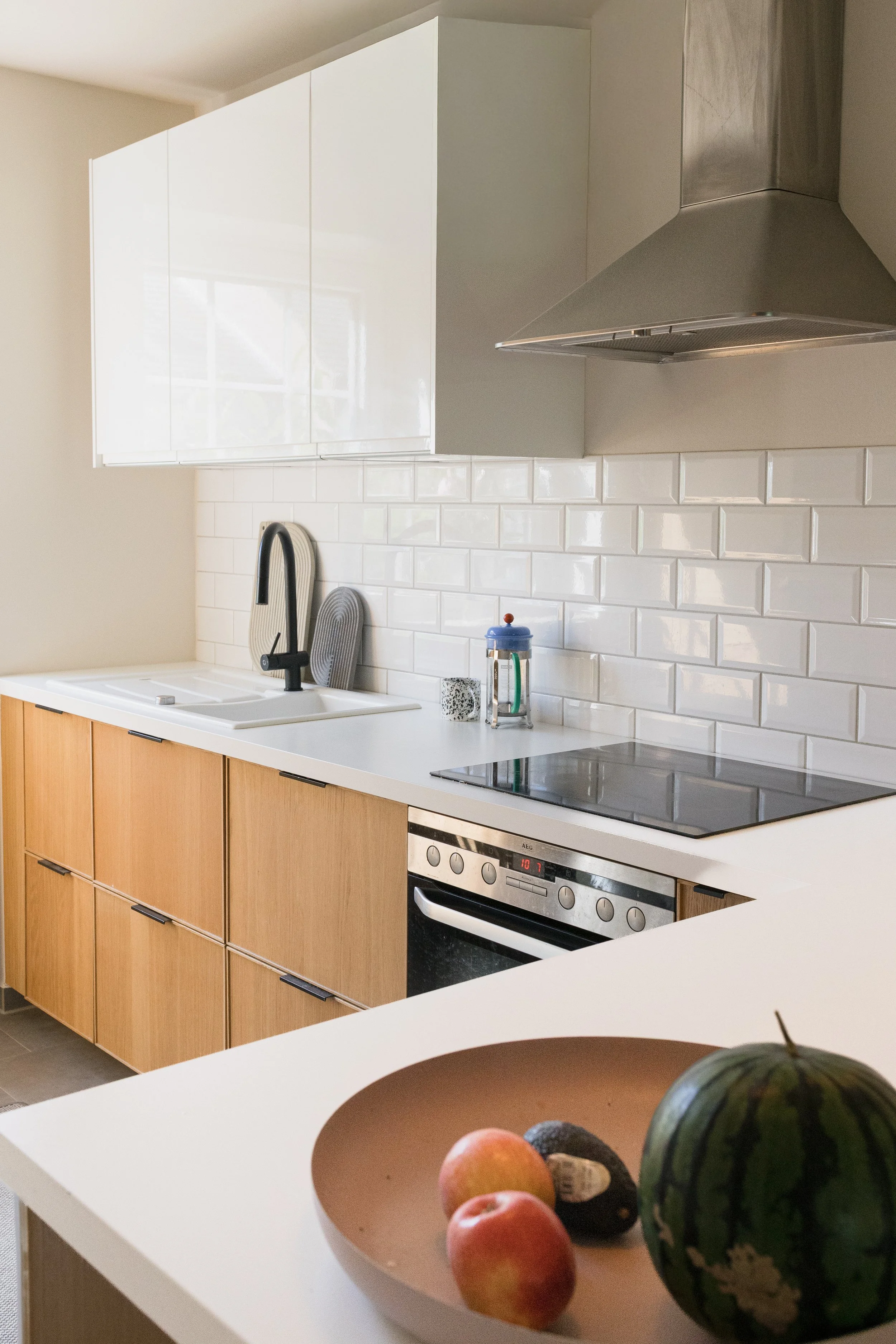 Moderne Küche mit warmen Holzfronten, weißen Arbeitsflächen und schwarzen Armaturen als Teil des ganzheitlichen Einrichtungskonzepts.