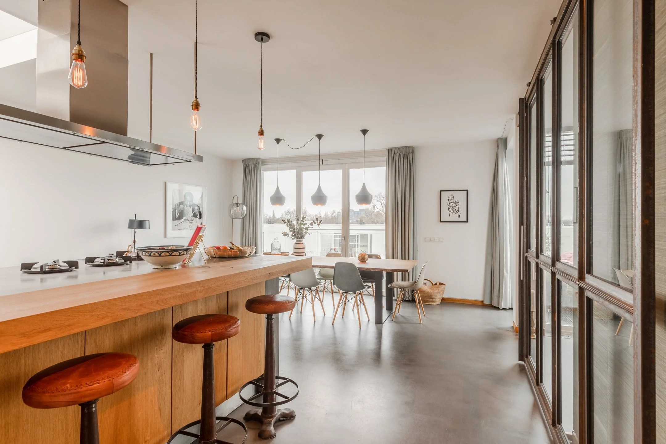 Blick durch den offenen Wohnbereich mit Kücheninsel, Esstisch und industriellen Glaselementen – Interior Design eines Penthouses in Amsterdam.