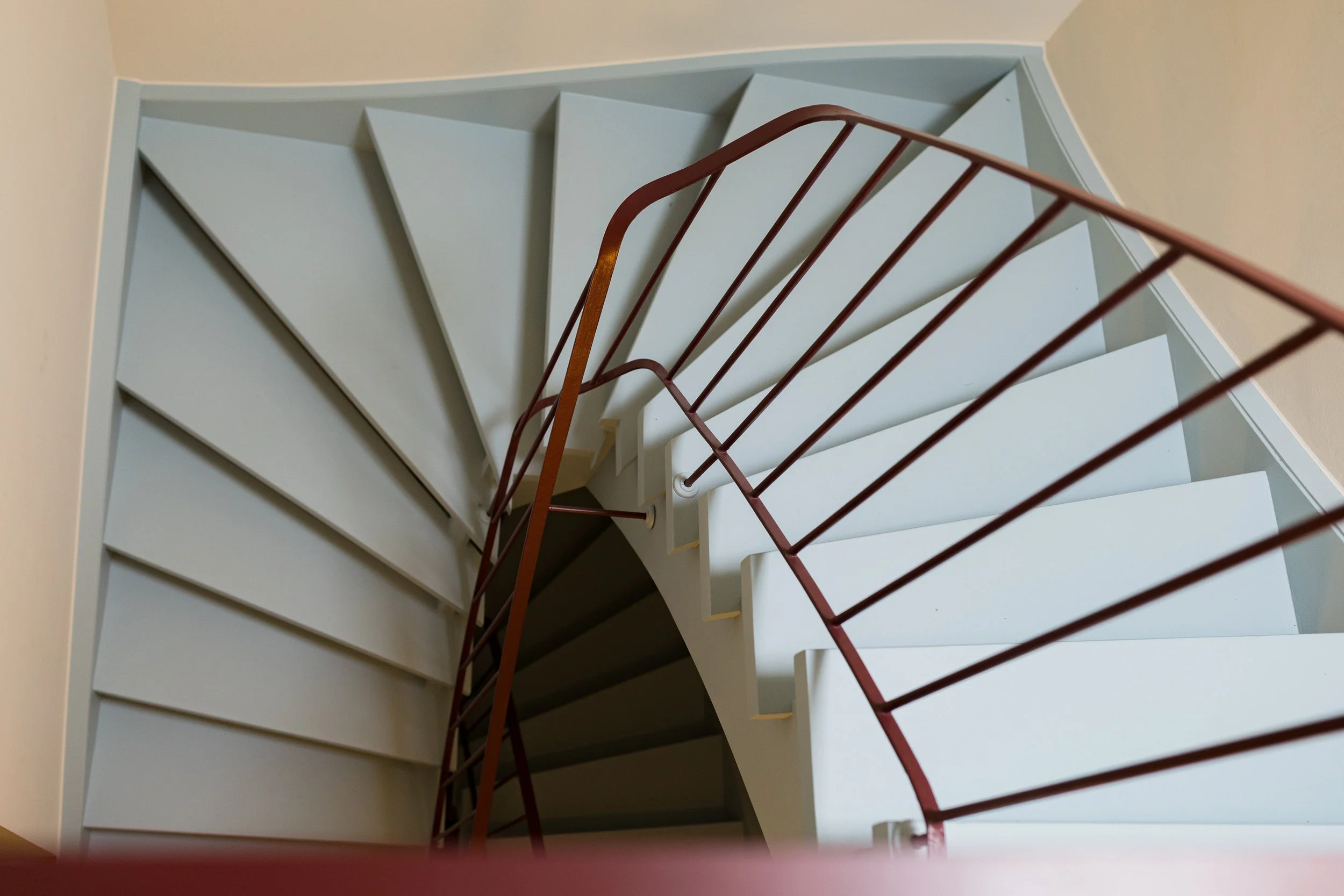 Charaktervolle Wendeltreppe mit hellblauen Stufen und rotem Geländer als Ausgangspunkt des Farbkonzepts im Reihenhaus in Hamburg-Rissen.