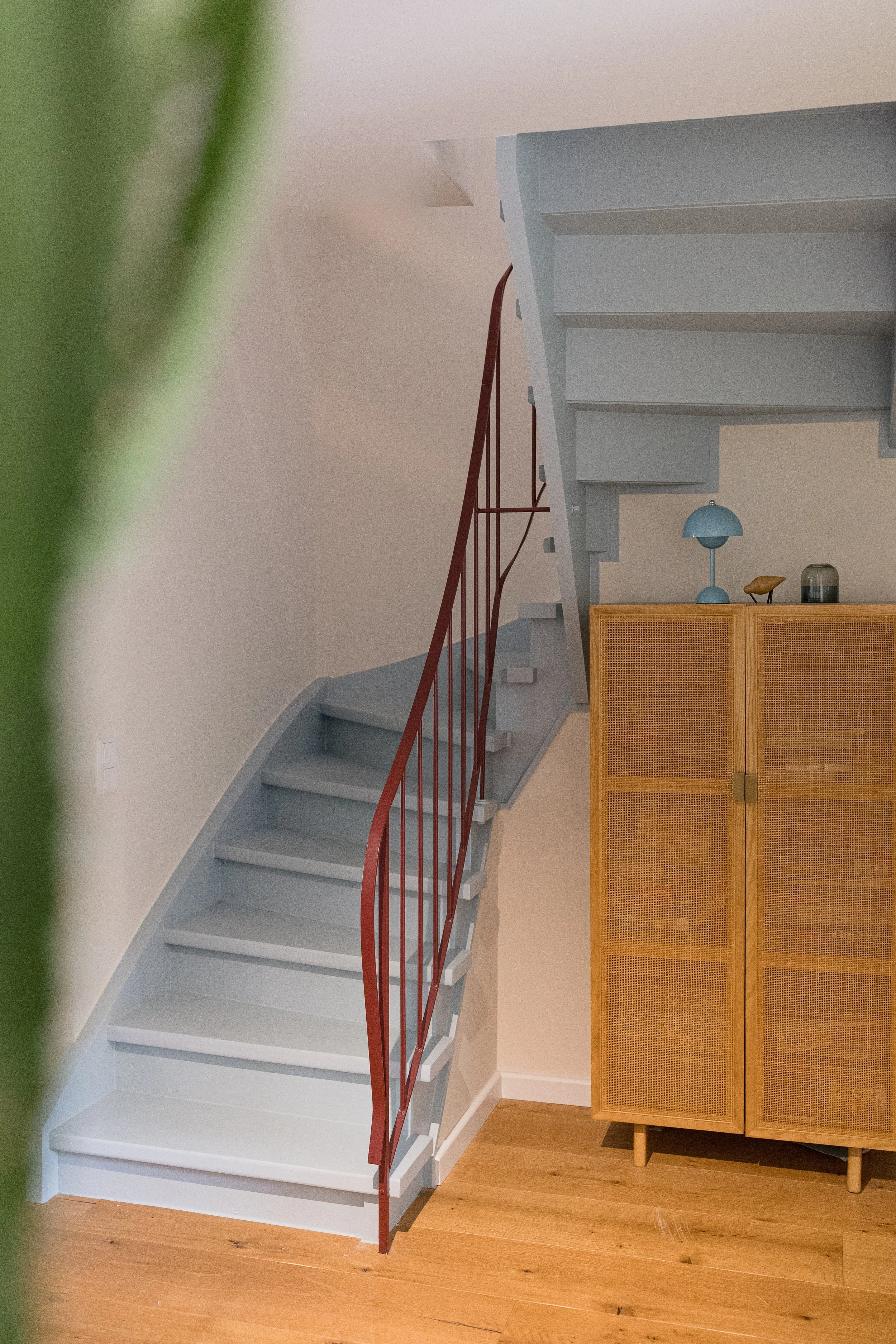 Treppenbereich mit hellblauer Treppe, rotem Geländer und Vintage-Schrank – individuelles Farbkonzept für ein Reihenhaus in Hamburg.