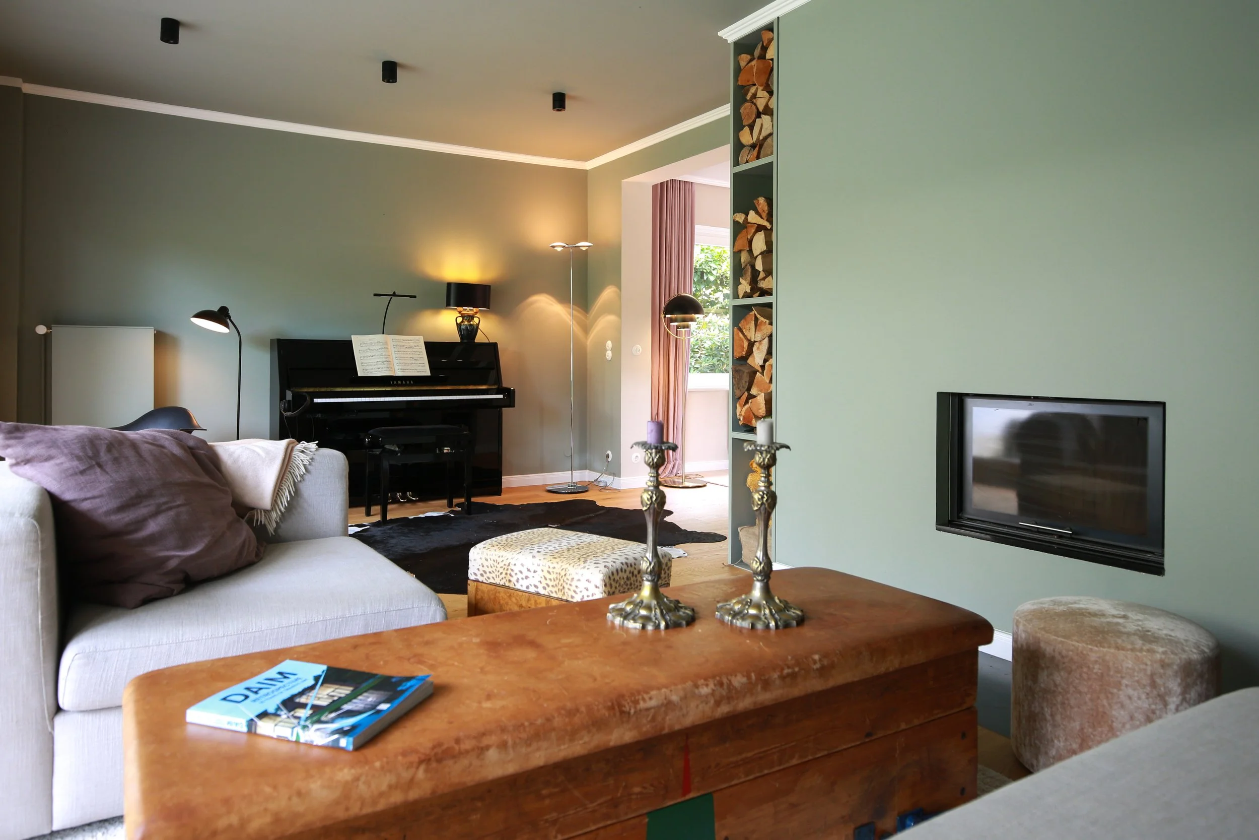 Wohnzimmergestaltung mit gedecktem Grün, integriertem Kamin, Klavier, Vintage-Möbeln und warmen Materialien – Interior Design in Hamburg.