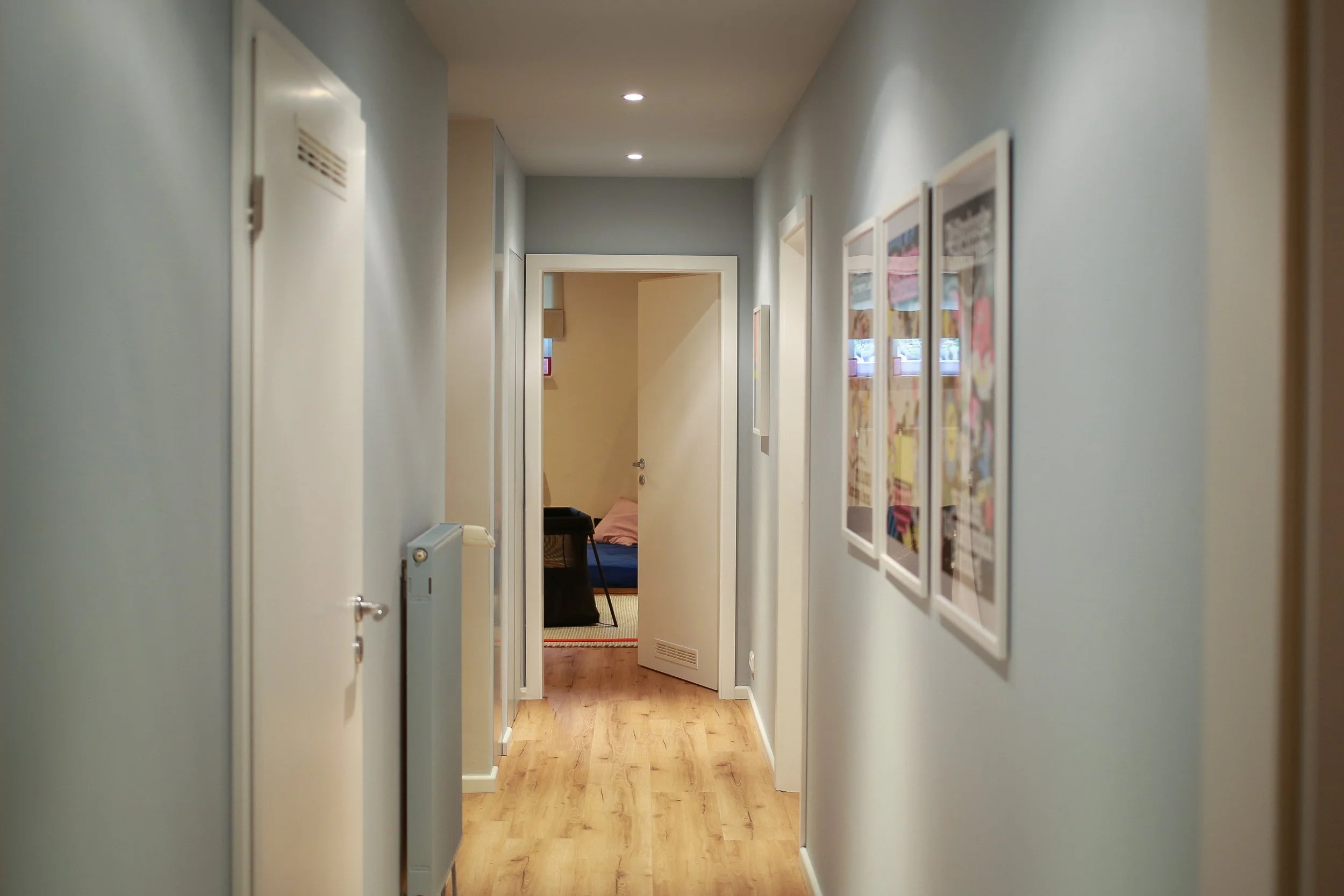 Komplett neu gestalteter Flur im Kinderkeller mit neuem Boden, sanftem Blau-Grau und farbiger Bilderwand – ein freundlicher Übergang zwischen den einzelnen Bereichen.