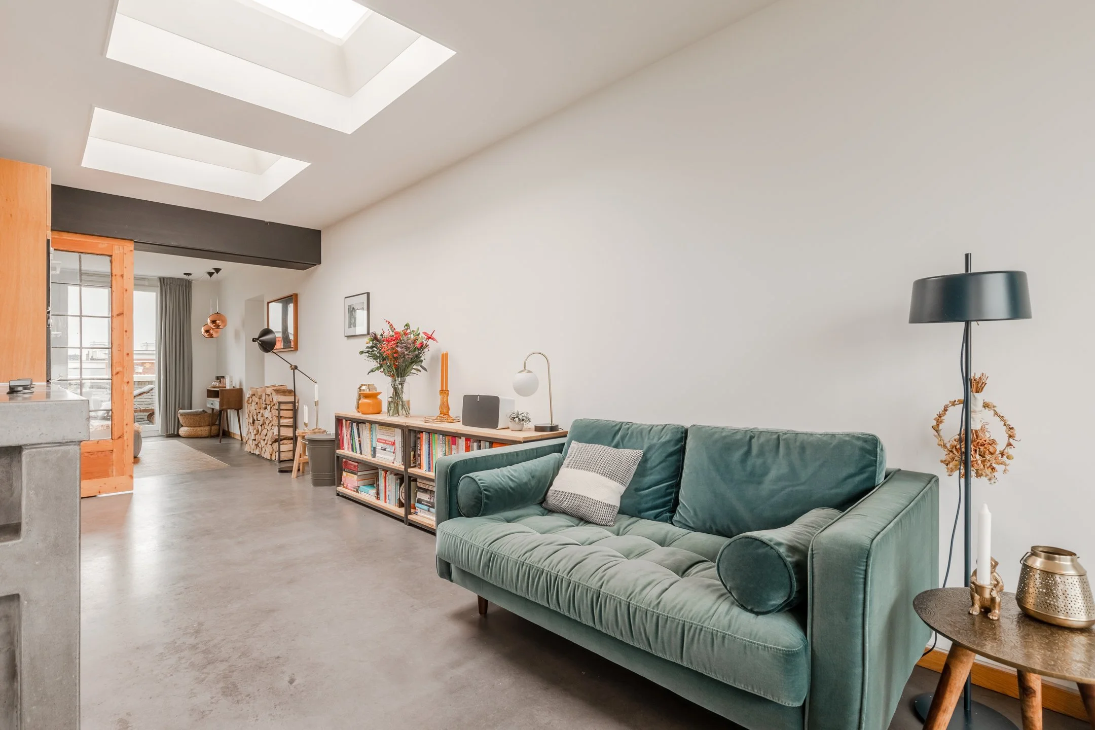 Wohnbereich mit petrolfarbenem Sofa, Betonboden und natürlichem Licht – moderner, warmer Materialmix im Penthouse in Amsterdam.