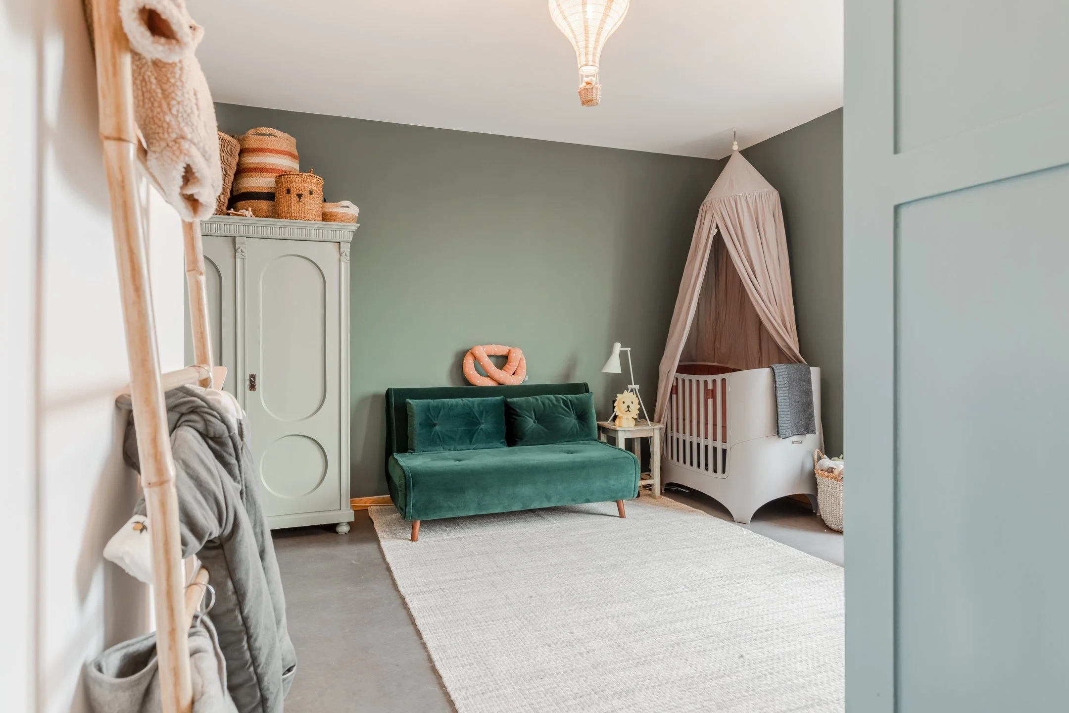 Kinderzimmer mit gedecktem Grün, Vintage-Schrank und Samtsofa – individuelles Farb- und Einrichtungskonzept.