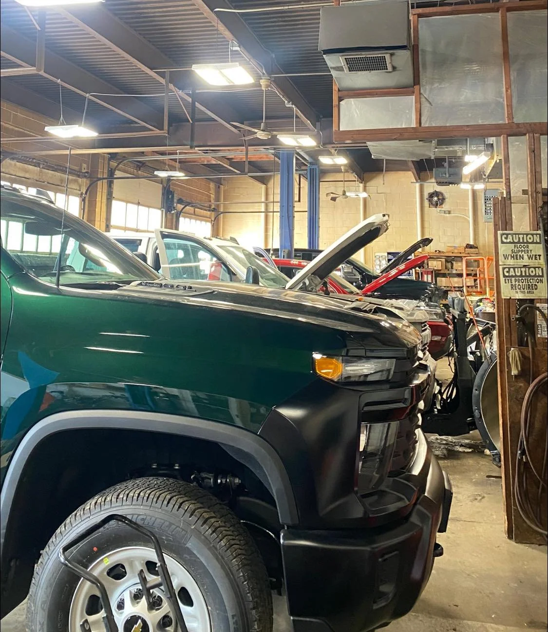 Inside an auto repair shop with multiple cars, some with hoods open, in a spacious industrial setting with high ceilings and lighting.