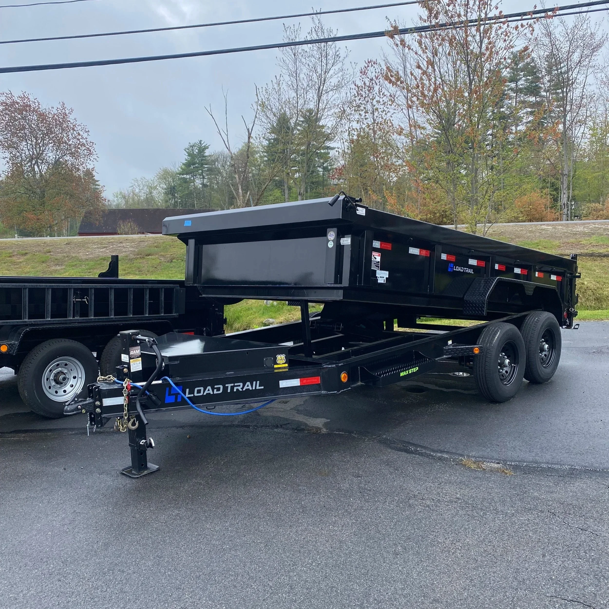 White GMC pickup truck with a raised metal dump bed, parked outside a building with signage for Candia Trailers & Snow Equipment Company.