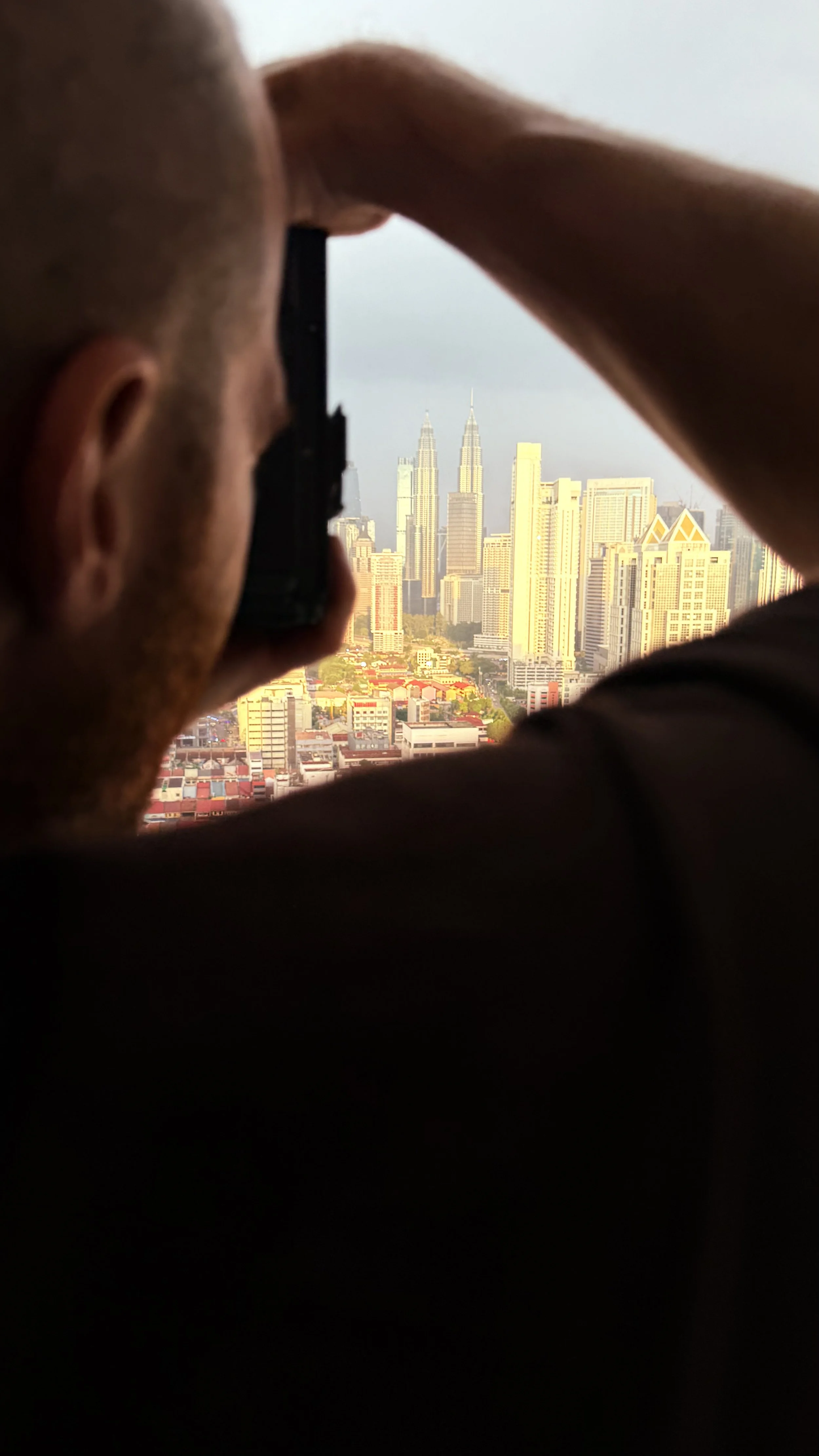 Erik van der Ven taking a photo of the city skyline, including the Petronas Towers, from a balkony.