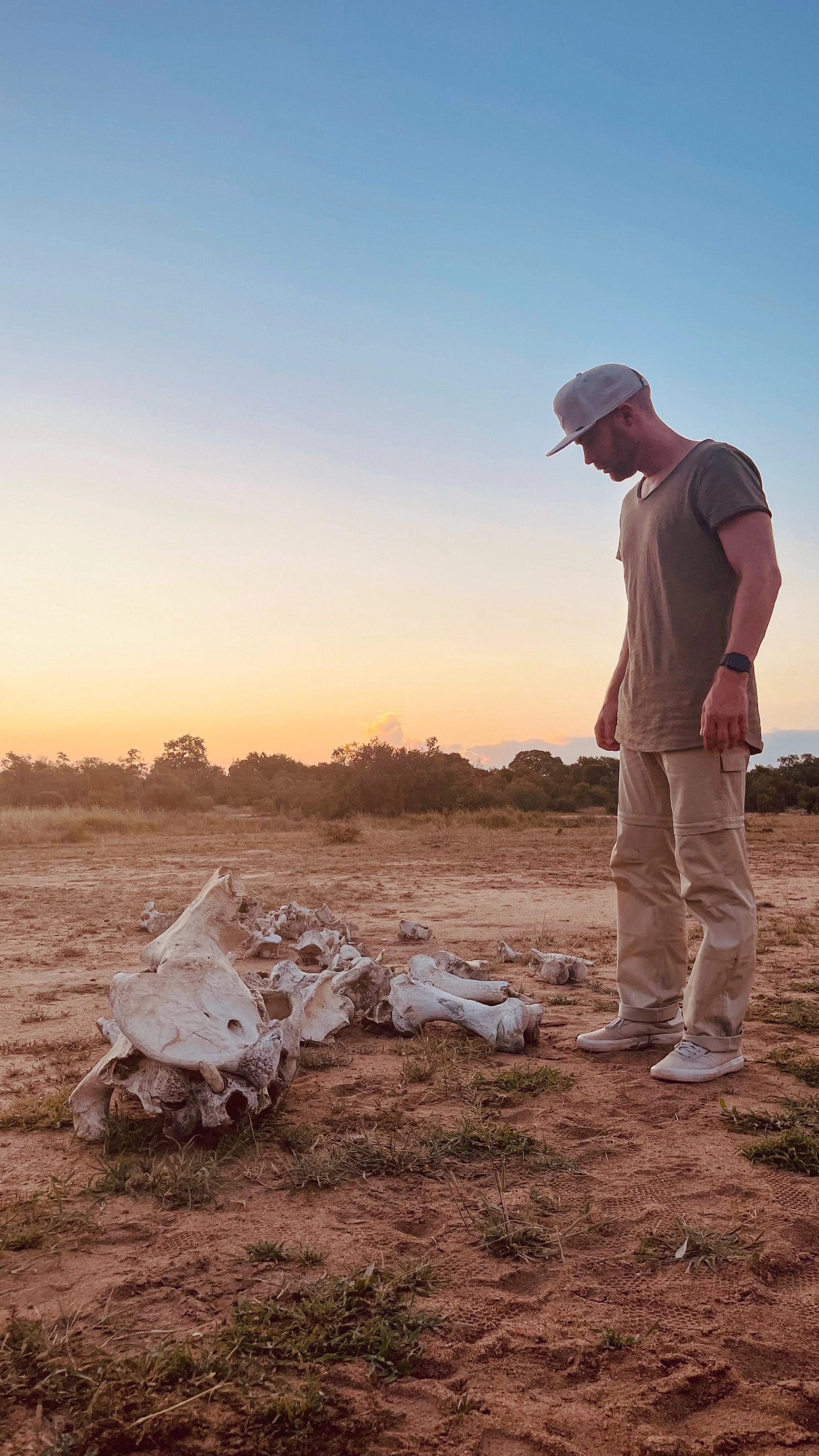 Erik van der Ven standing outdoors on a dirt terrain with animal bones on the ground, during sunset, looking down at the bones.
