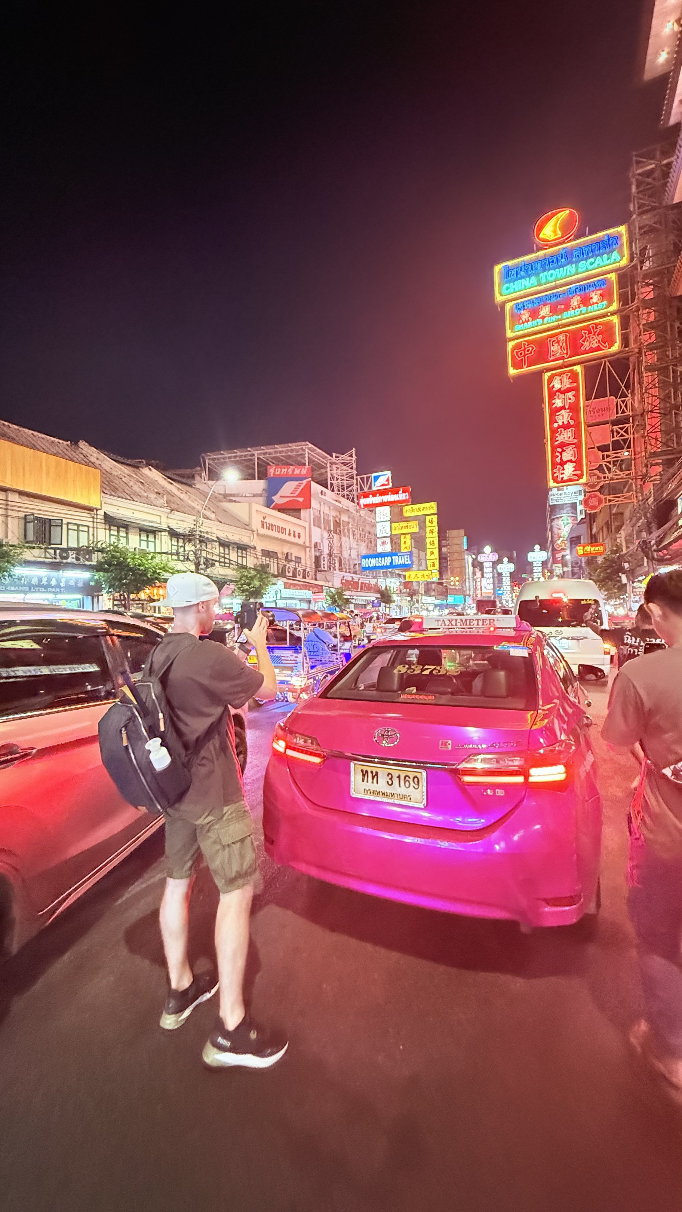 Nighttime street scene with neon signs in Chinese characters, cars, and pedestrians, including Erik van der Ven taking a photo.
