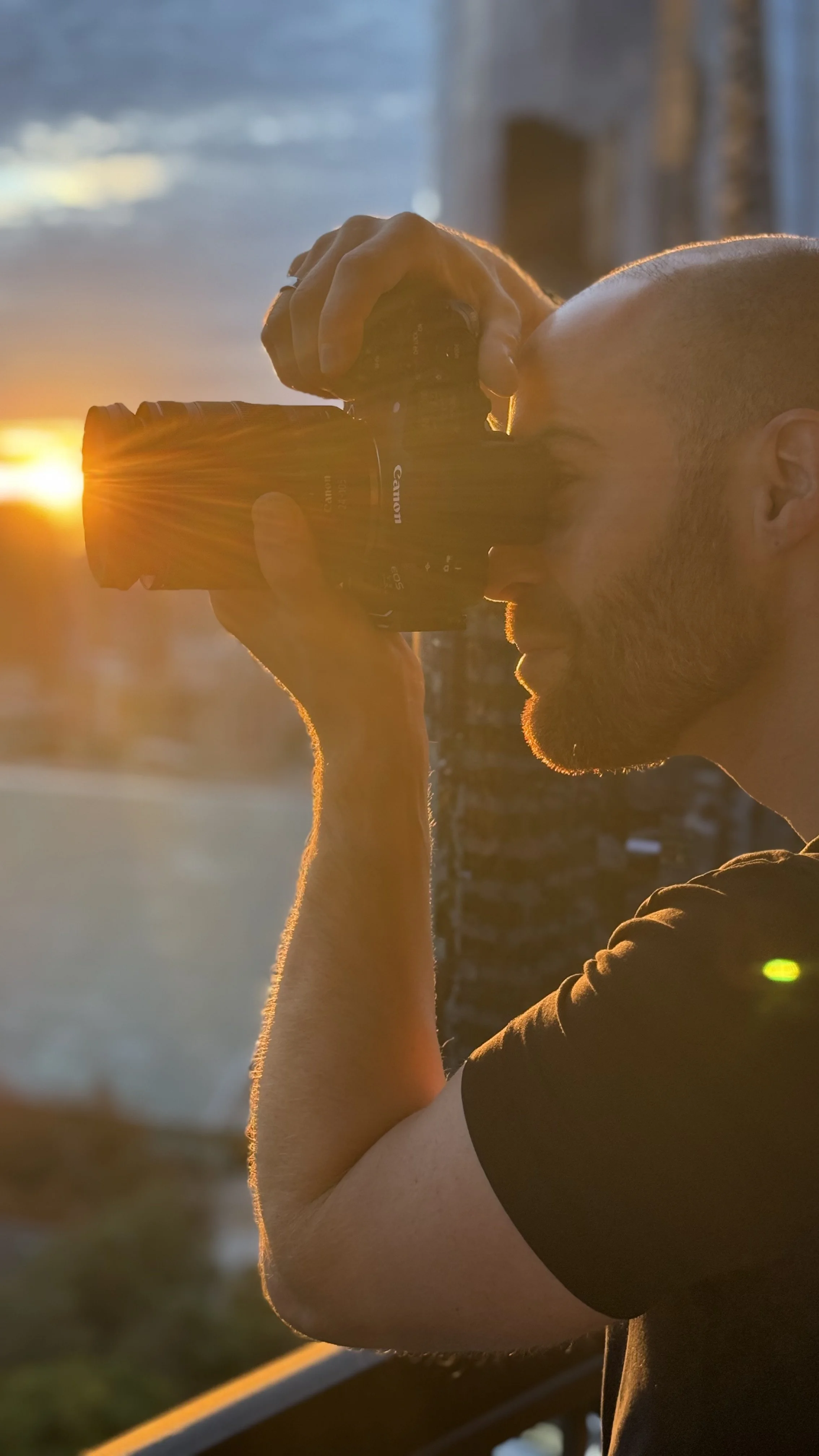 Erik van der Ven with a shaved head taking a photo with a Canon camera during sunrise.