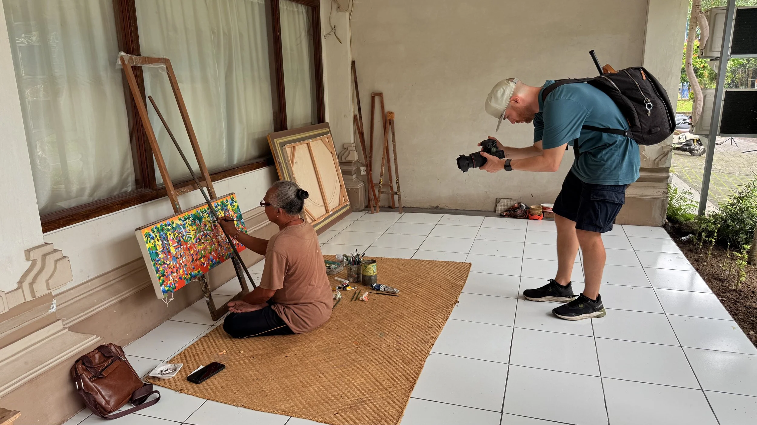 An artist is painting a colorful, abstract piece on a canvas outdoors, while a Erik van der Ven captures the moment.