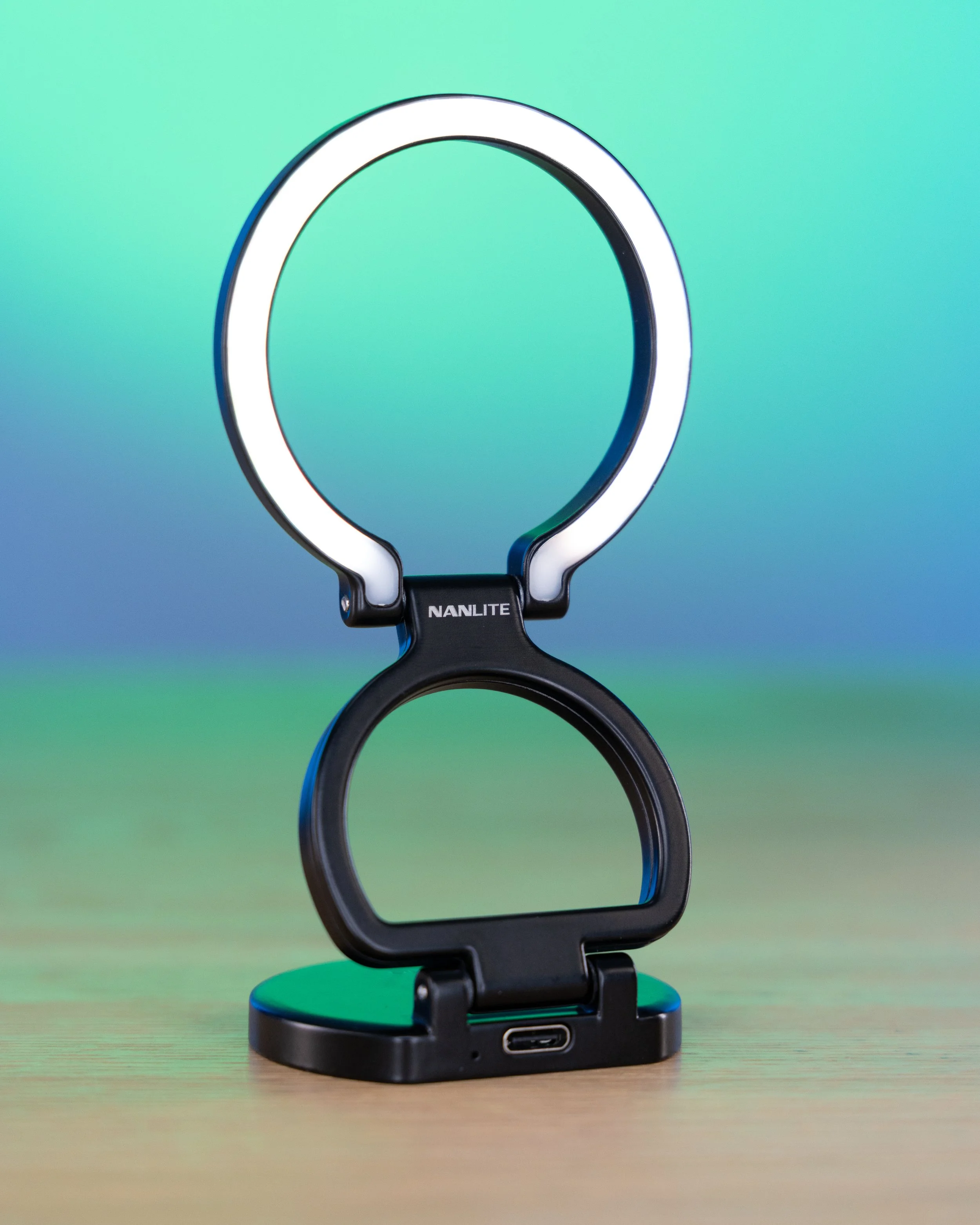 A circular ring light with the brand 'NANLITE' on a black stand, standing on a wooden surface against a gradient background.