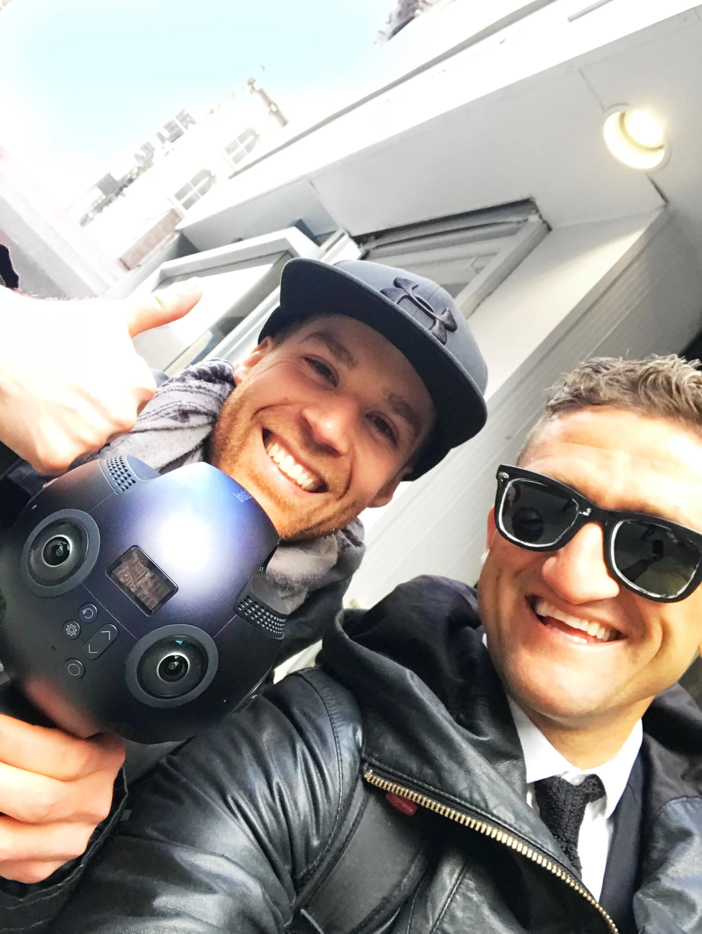 Erik van der Ven smiling taking a selfie withe Casey Neistatt outdoors, one wearing a black leather jacket and glasses, the other wearing a dark baseball cap and smiling broadly.