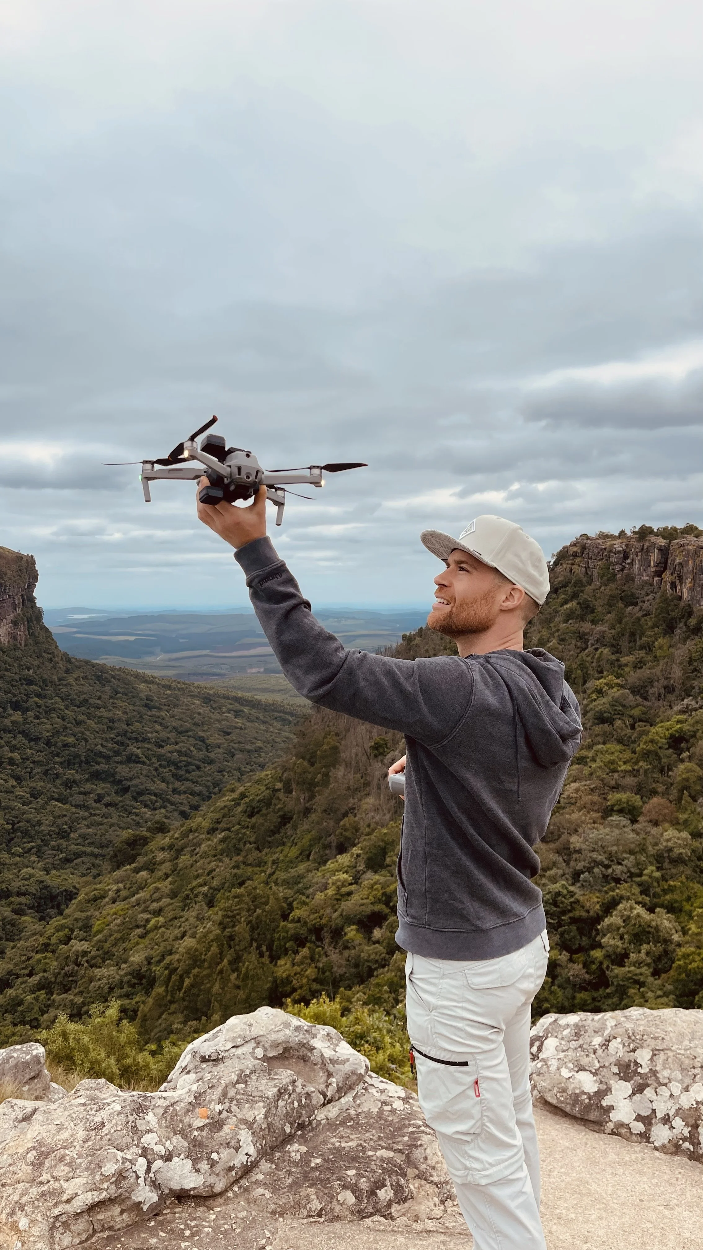 Erik van der Ven holding a drone on a mountain with scenic view of trees, hills, and a cloudy sky