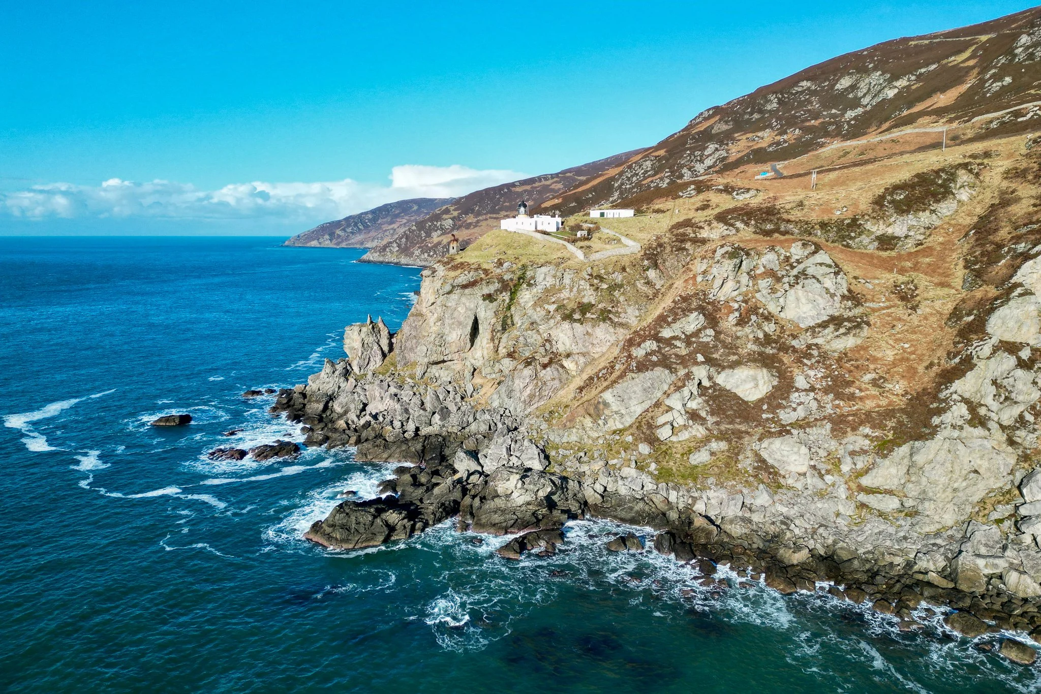 Cliffside ocean view with white buildings on top of the cliffs and rocky shoreline in the foreground.