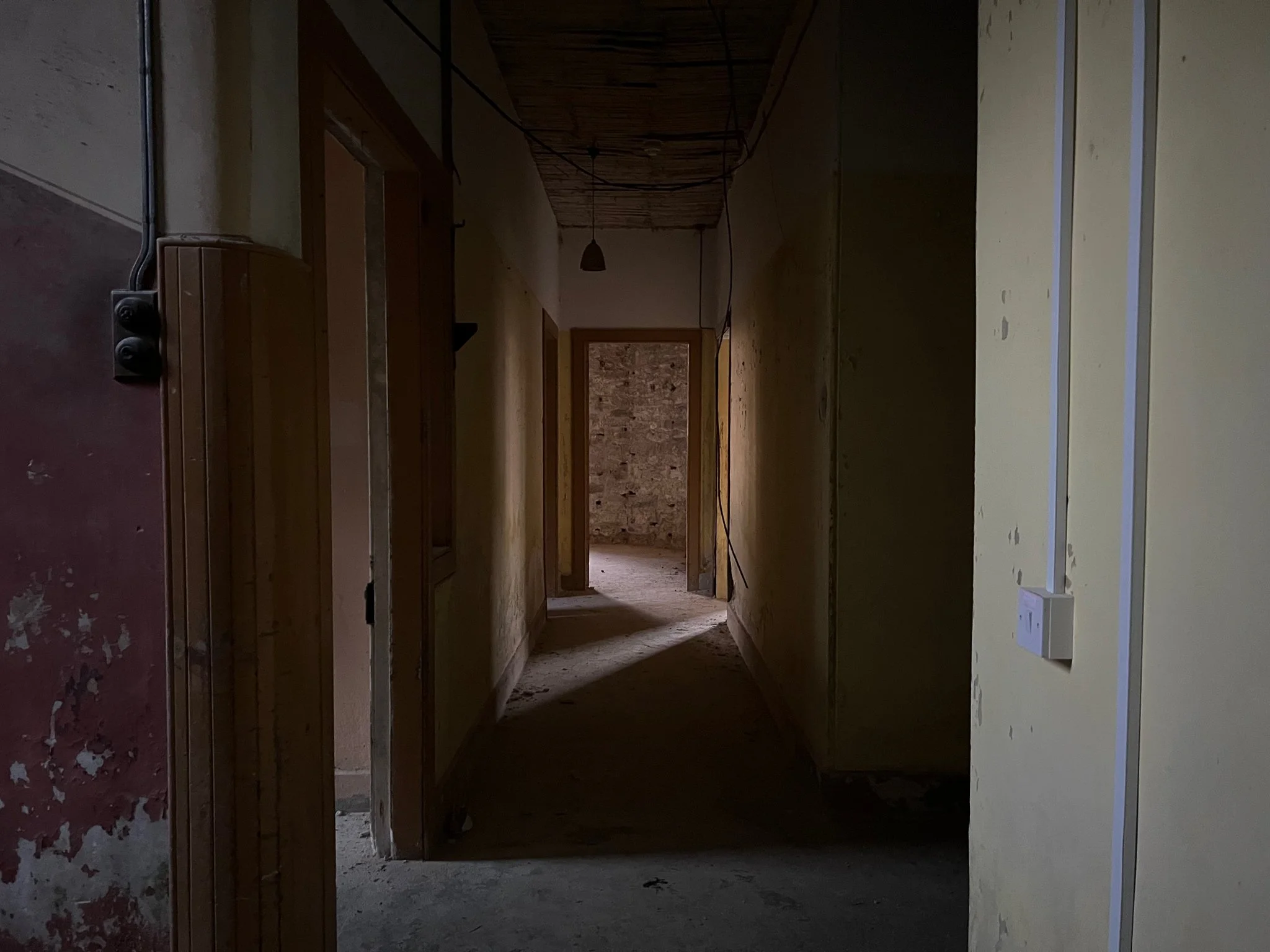 A dark, empty hallway with unfinished walls and exposed wiring, leading to a brick wall at the end.