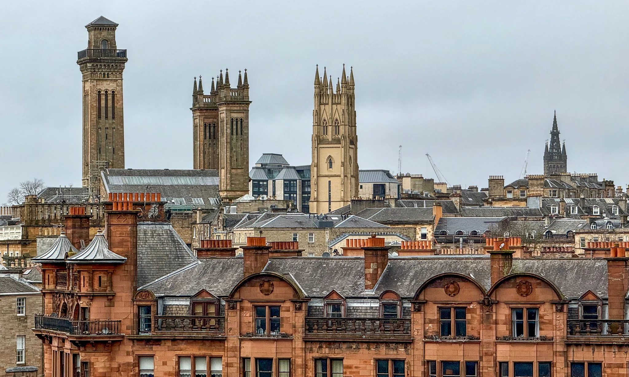 A cityscape featuring historic buildings with church steeples and towers, viewed on a cloudy day.