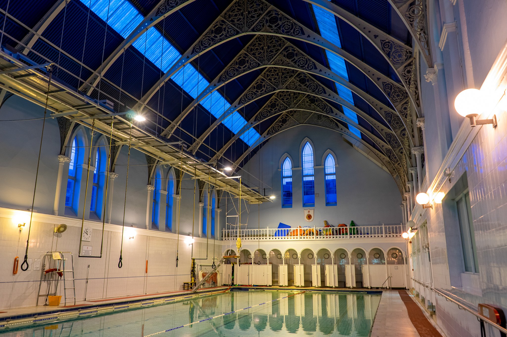 Indoor swimming pool with blue stained glass windows and decorative arched ceiling, illuminated by warm wall lights.