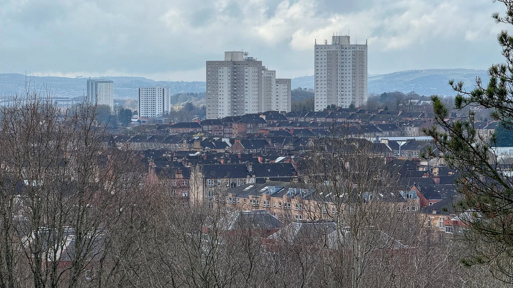 Cityscape with residential houses in the foreground and tall apartment buildings in the background under cloudy sky.