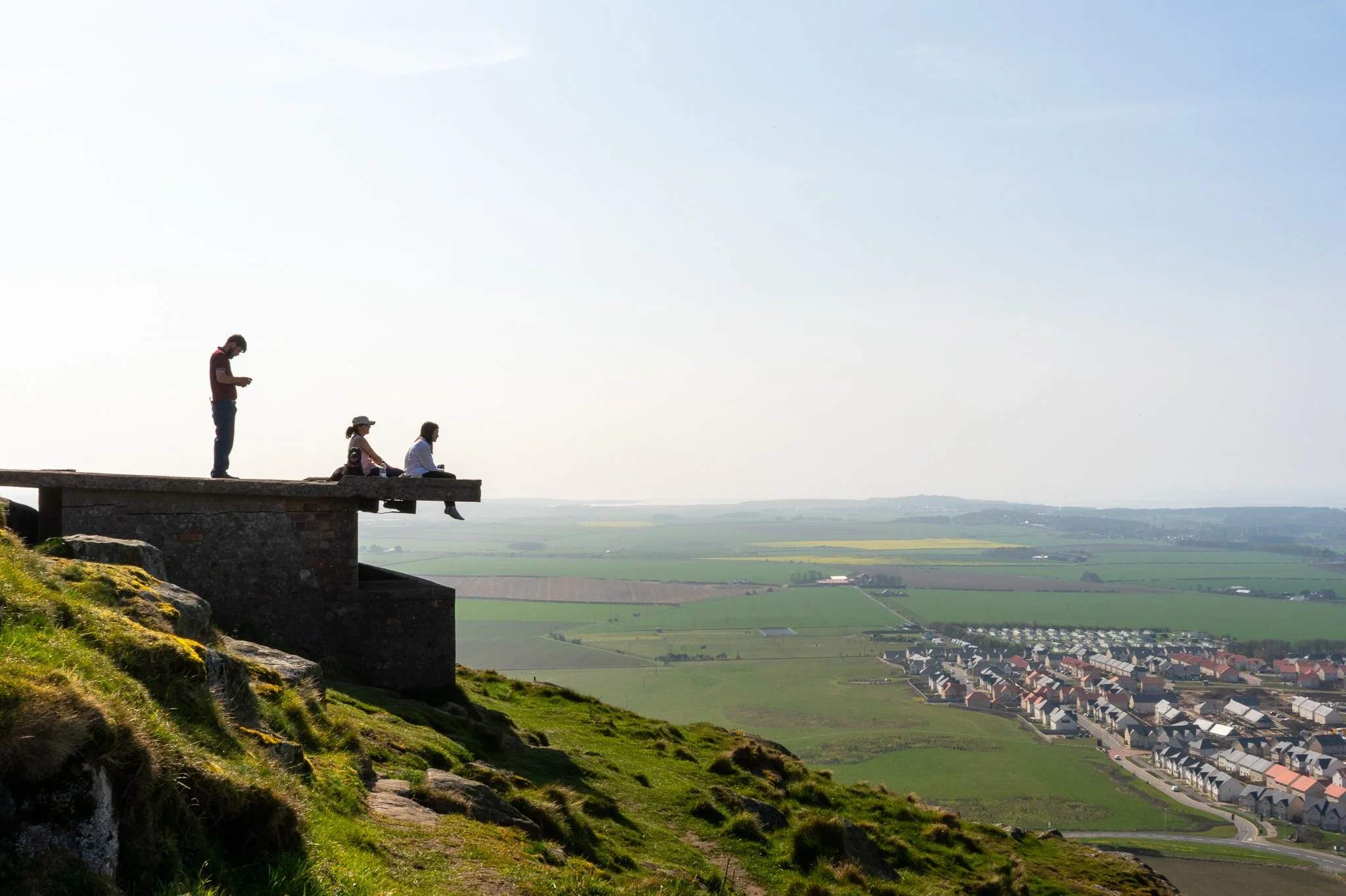 Four people on a viewing platform overlooking a valley with fields and a residential neighborhood.