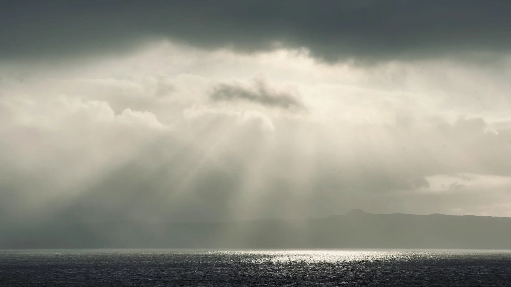 Overcast sky with sunlight breaking through clouds over the ocean.
