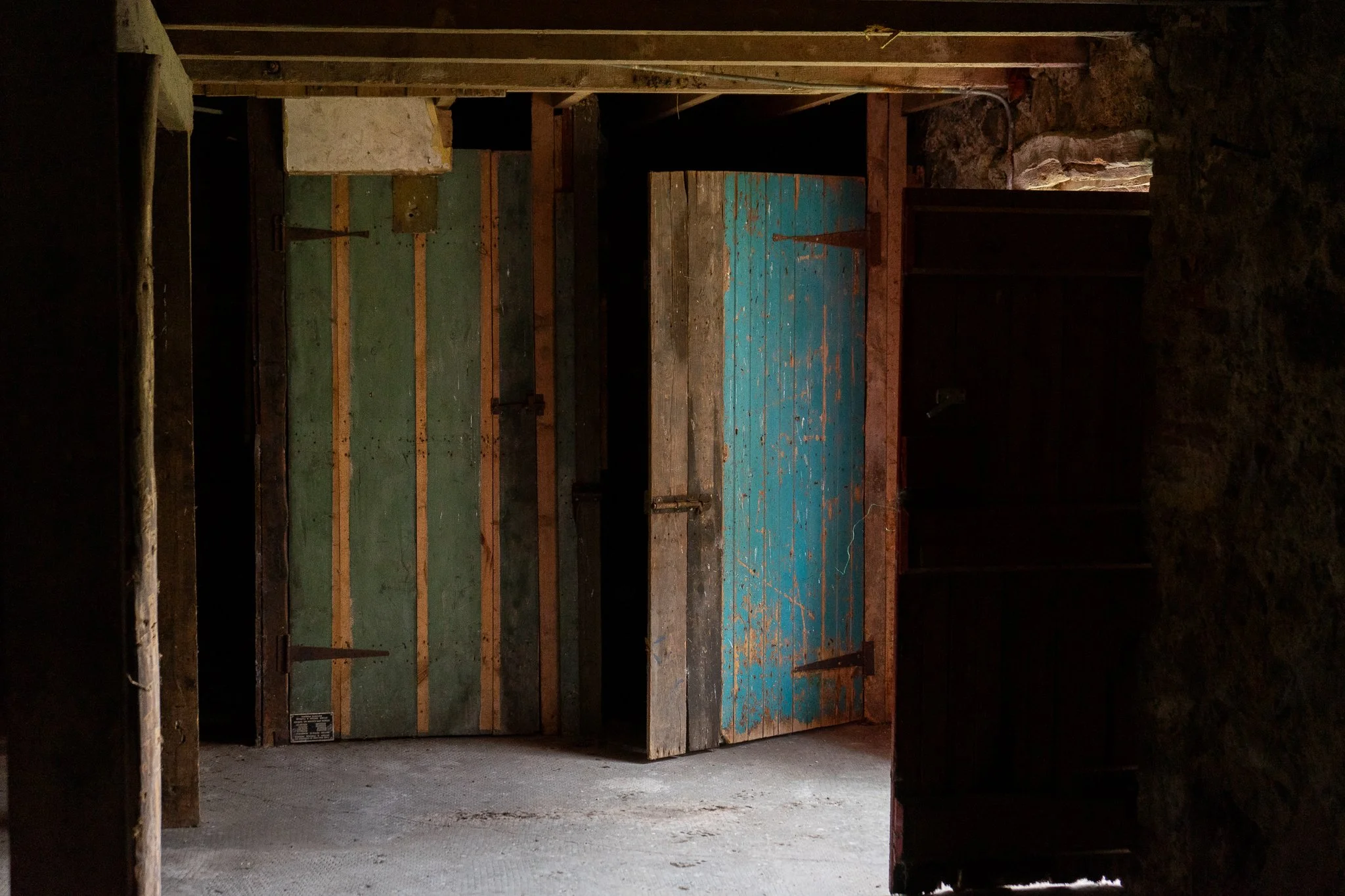 An old door with chipped blue paint opening into a dark, rustic room with wooden walls and stone accents.