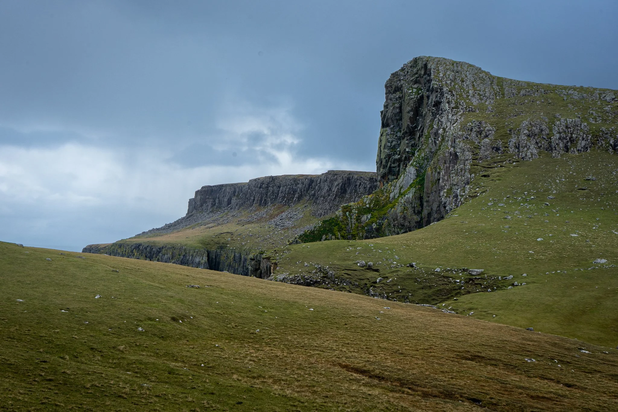 Scenic landscape of green rolling hills and rugged cliffs under a cloudy sky.