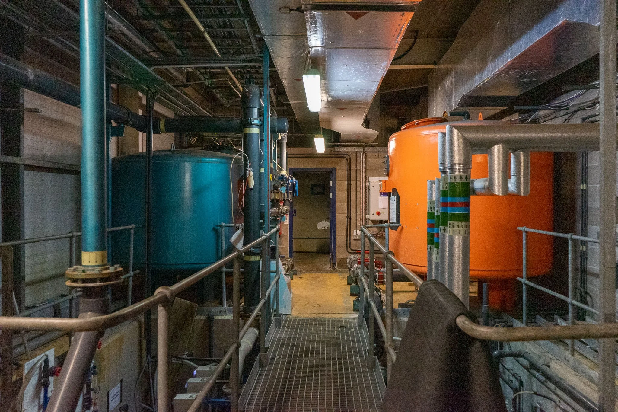 Industrial room with blue and orange tanks, pipes, and control panels.