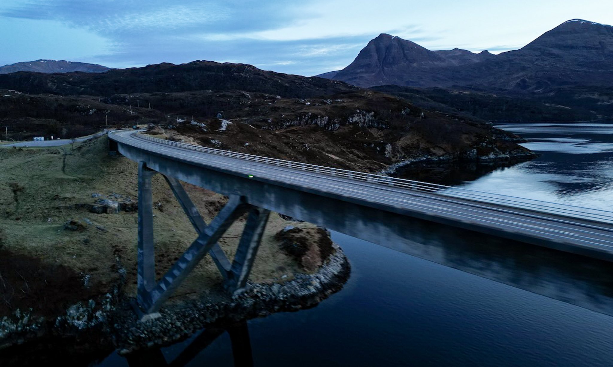 A large bridge over water with mountains in the background during dusk or dawn.