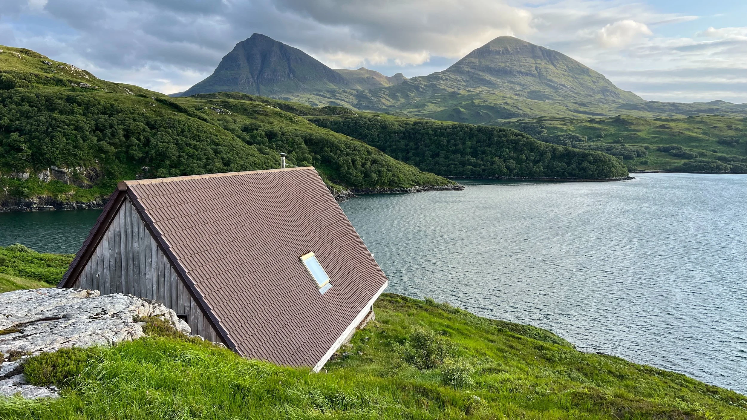 Timber cabin beside Loch Glencoul with Quinag mountains in the background, Scottish Highlands