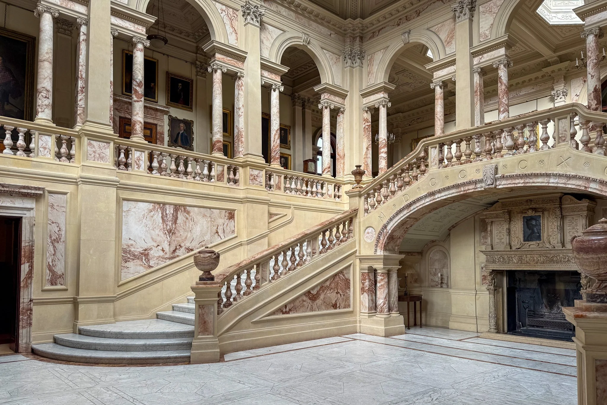 Luxurious interior of a historic mansion or palace with marble staircase, ornate columns, and decorative architecture.