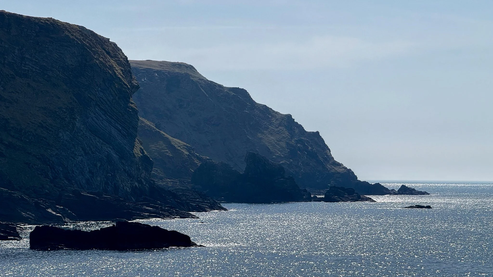 Cliffs by the sea with dark rocks and shimmering water in the sunlight.