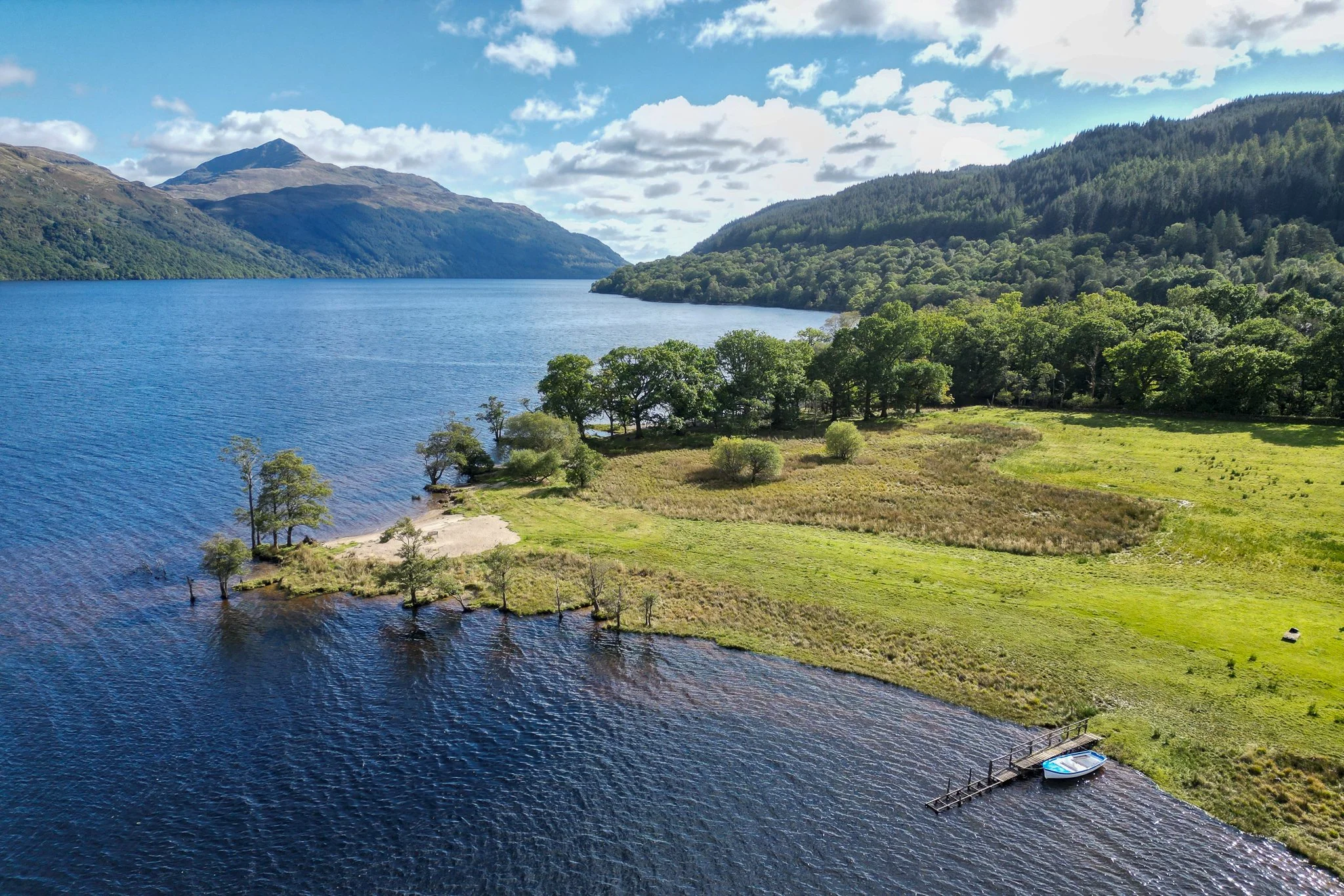 Aerial view of a lake surrounded by mountains and green trees, with a small dock and a boat.