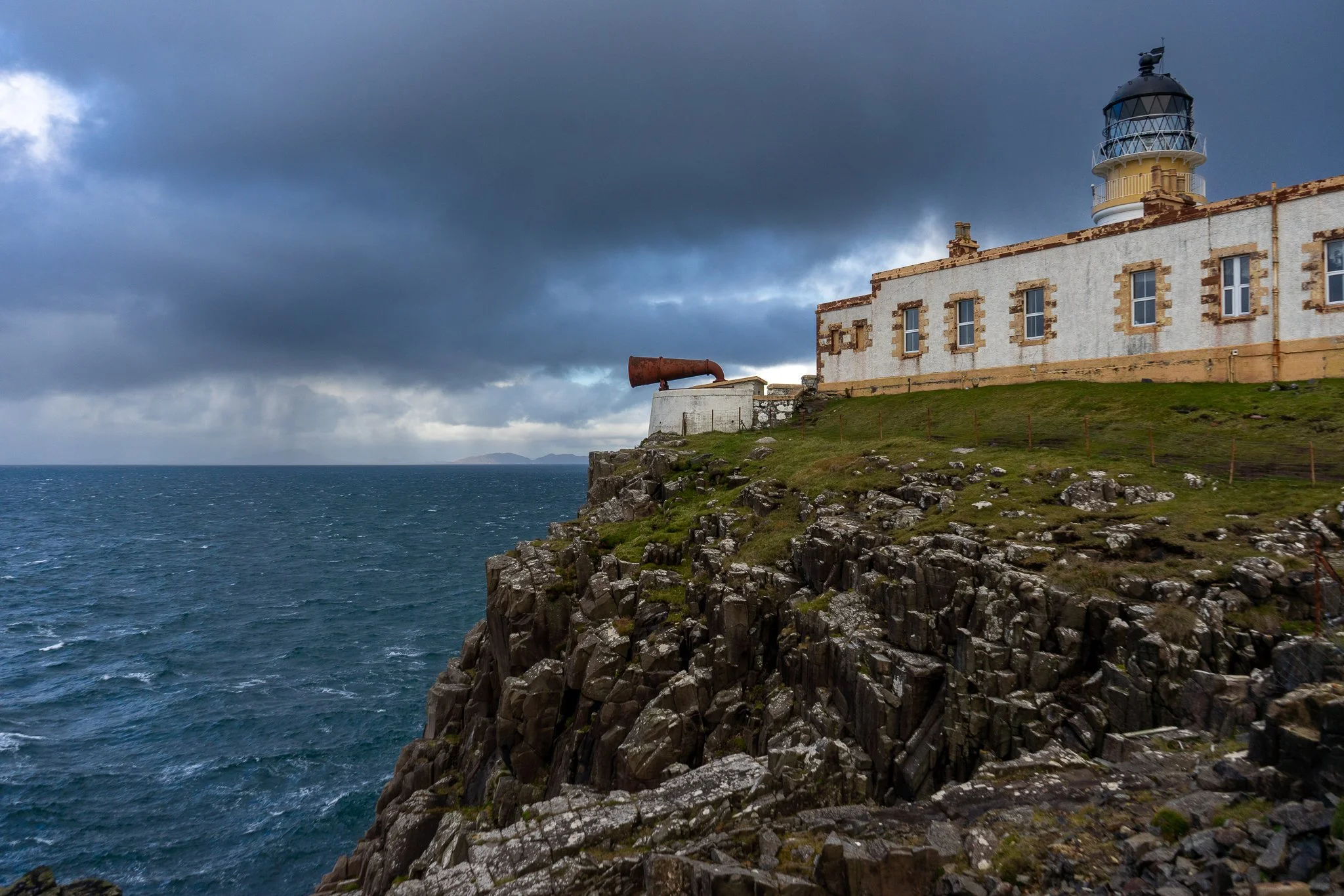 A lighthouse on a rocky cliff near the ocean, with a cloudy sky overhead.