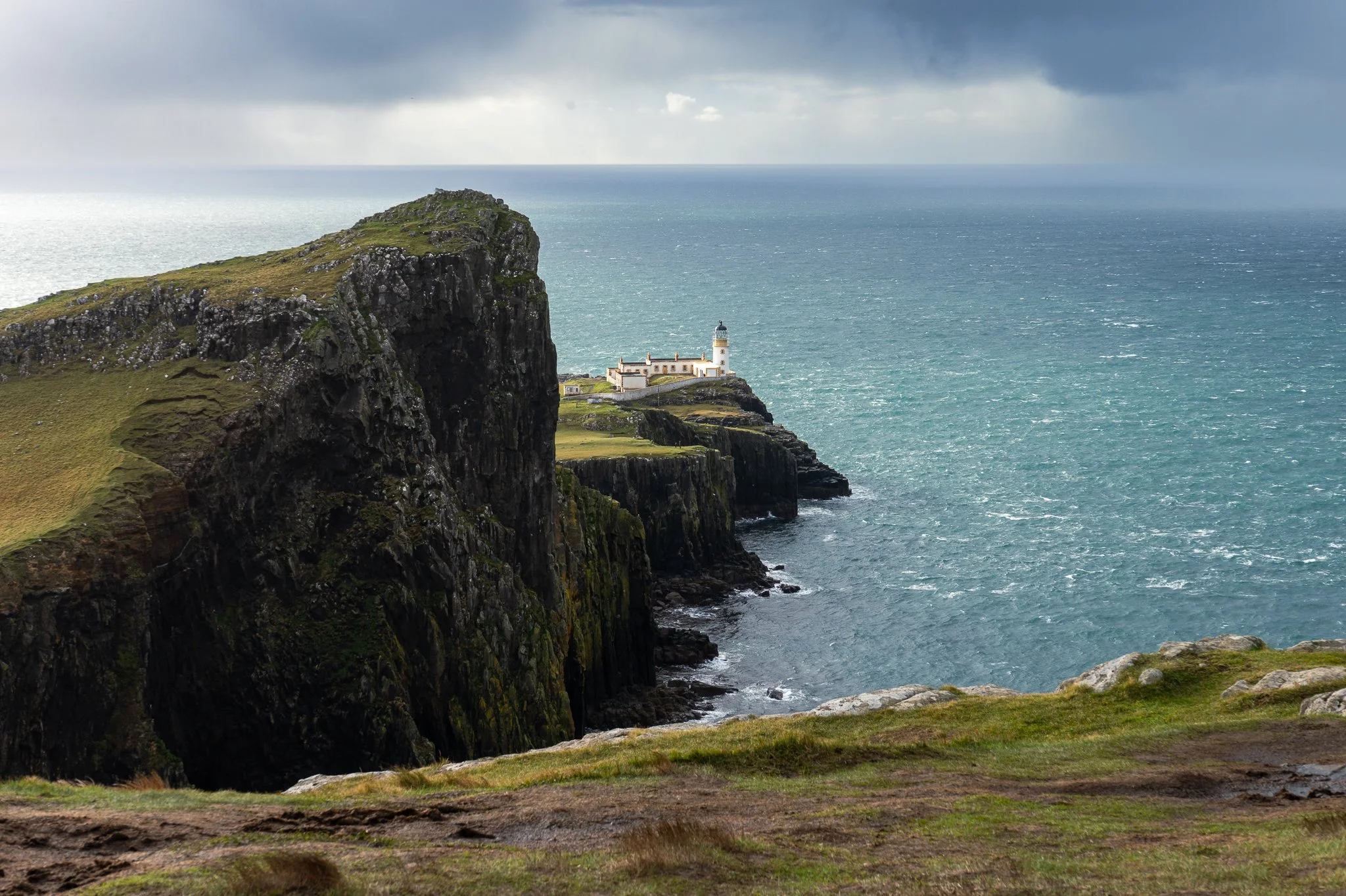 A lighthouse on a cliff overlooking the ocean with dark clouds in the sky.