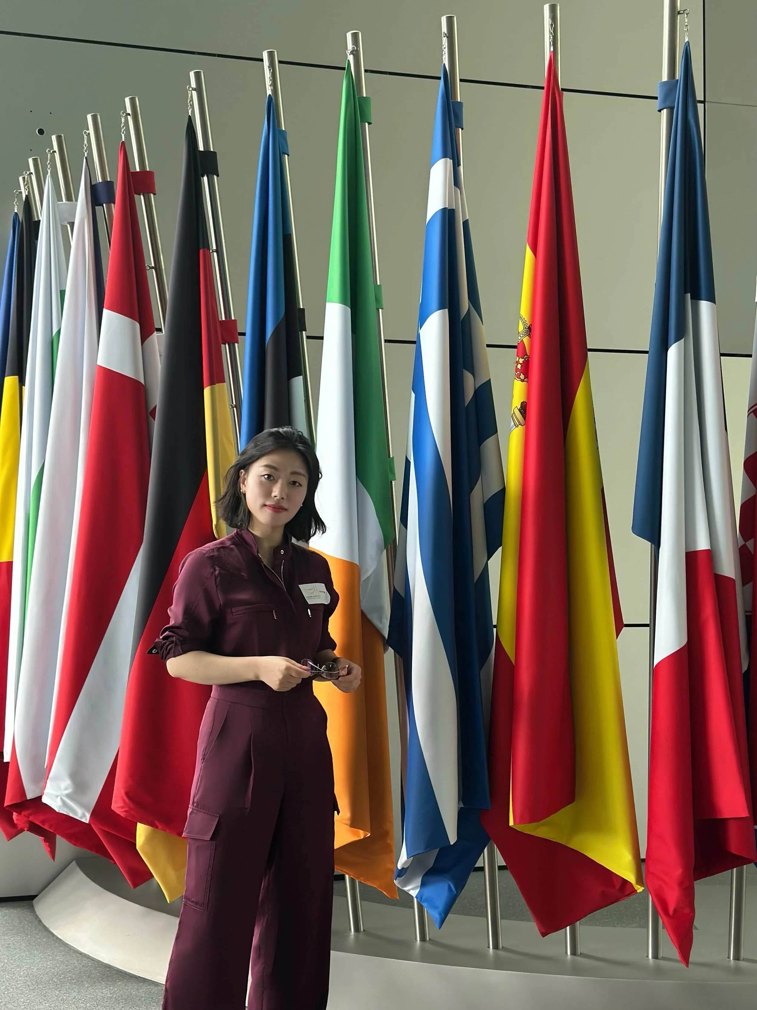 Frau steht vor einer Reihe von internationalen Flaggen in einem modernen Gebäude.