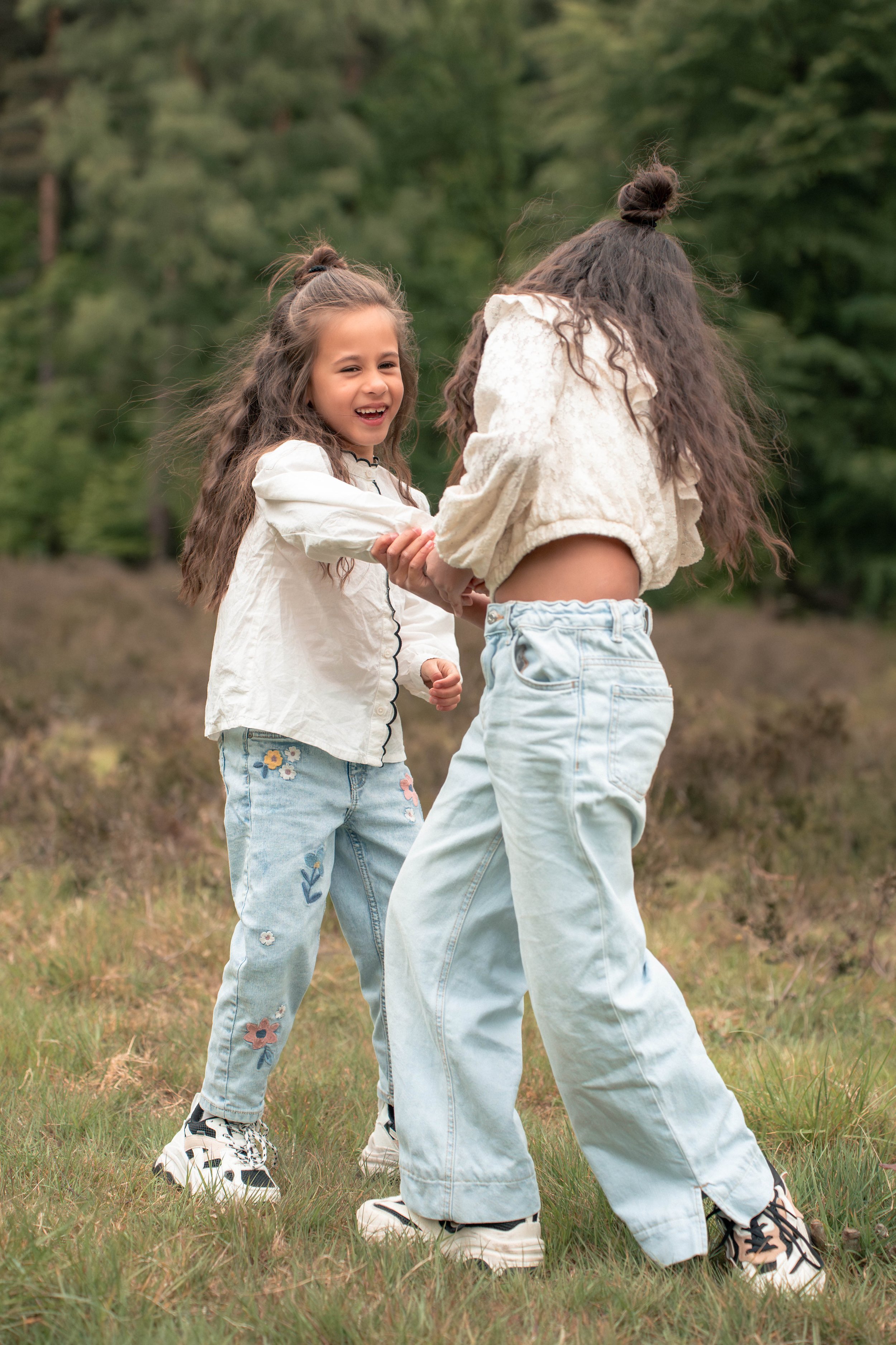 Twee meisjes die lachen en hand in hand lopen in een bosrijke omgeving.