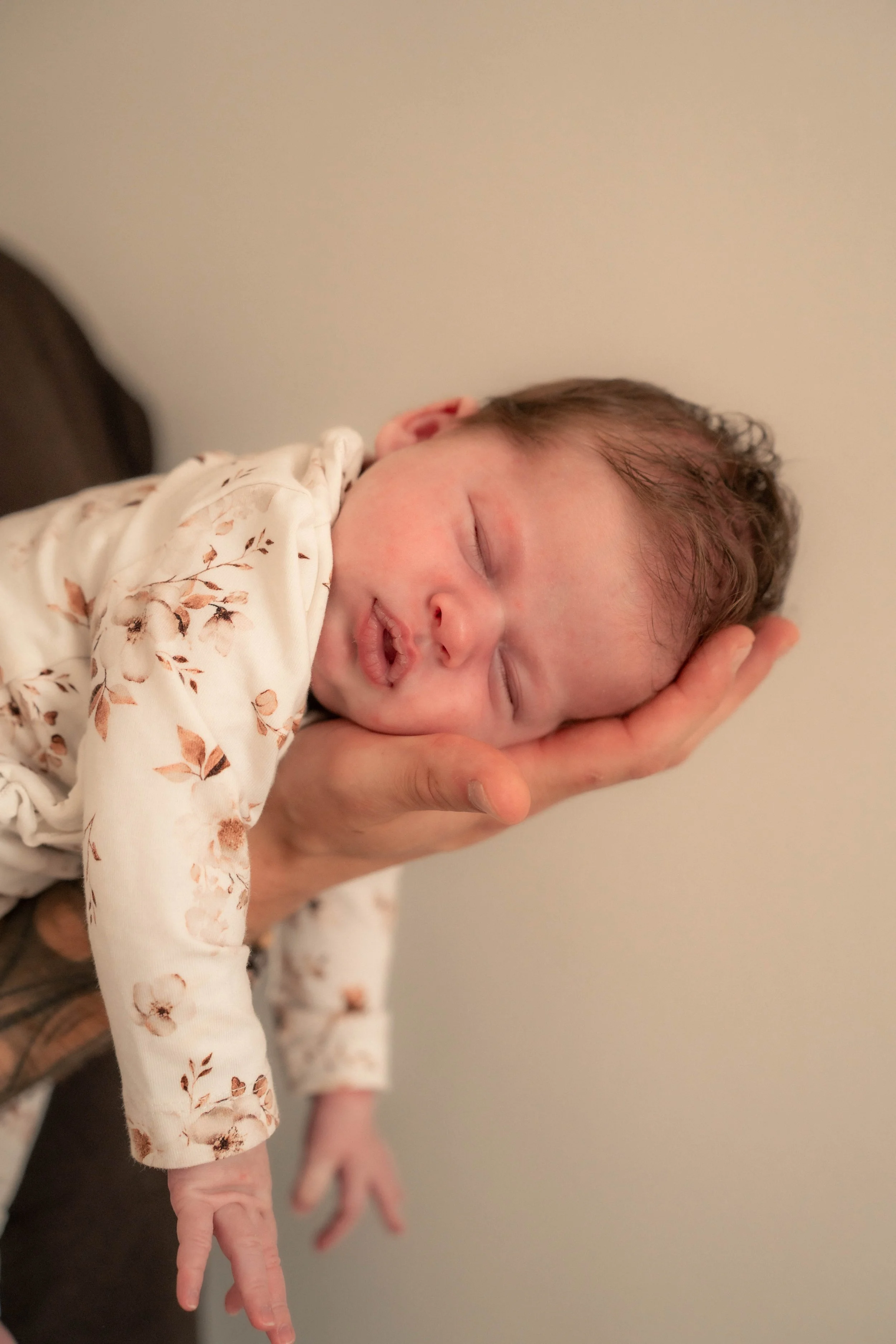 Close-up van een slapende baby met open mond, gedragen door een volwassene die een hand onder het hoofd van de baby houdt.