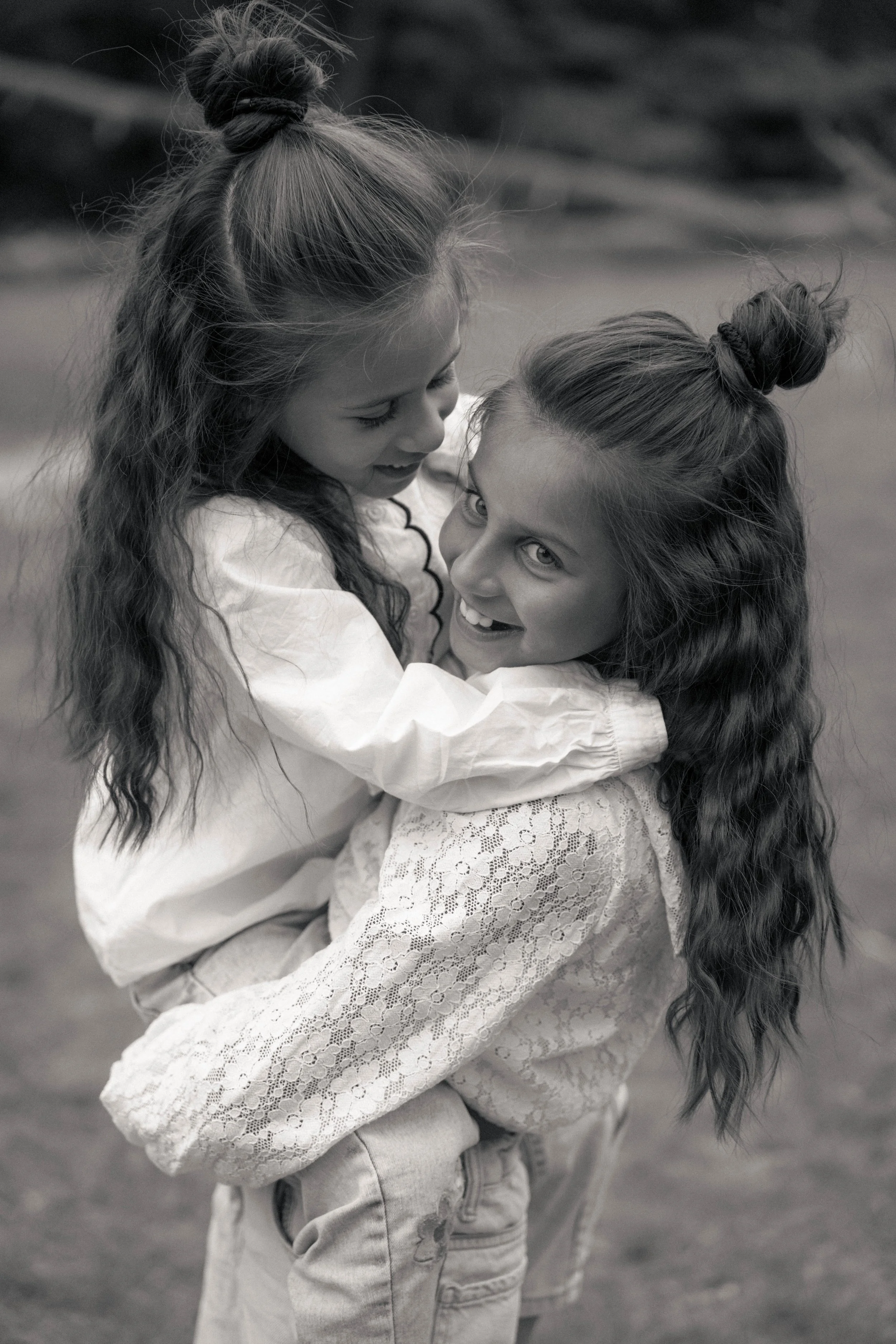 Twee jonge meisjes met lang haar in een omhelzing en lachend, in een zwart-wit foto.