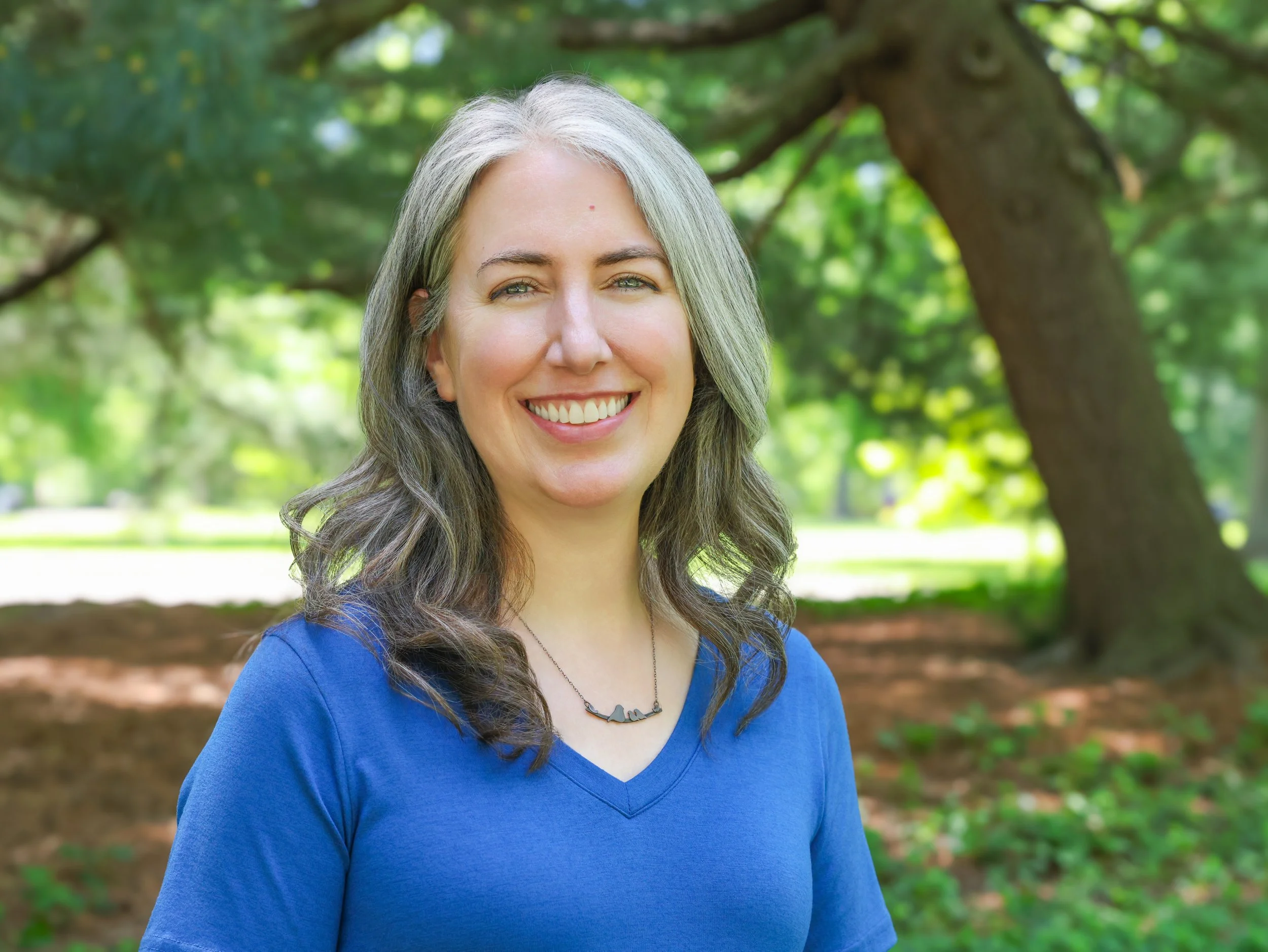 Kathleen Robbins, a postpartum doula in St. Louis, sits in a park with a tree behind her.