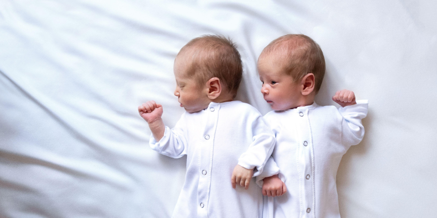 Newborn twin babies wearing white pajamas.